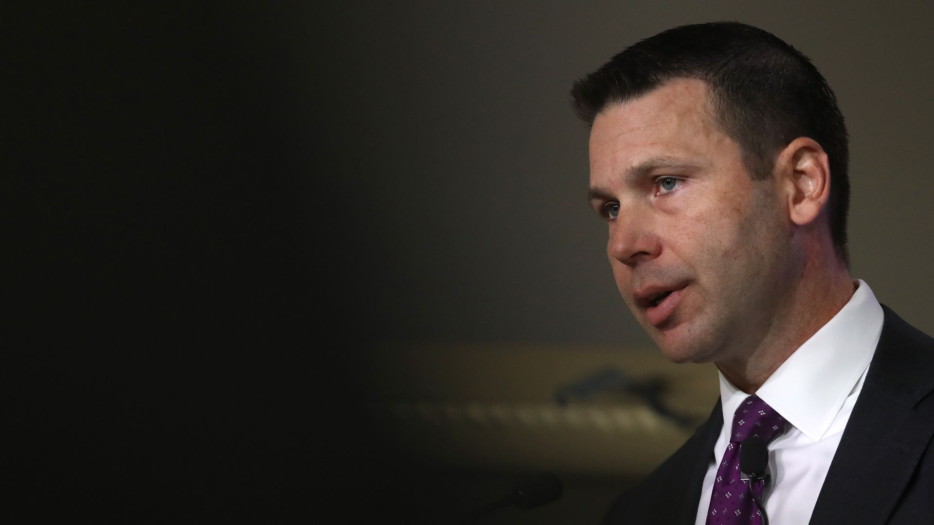 In this image, Kevin wears a suit and tie and speaks