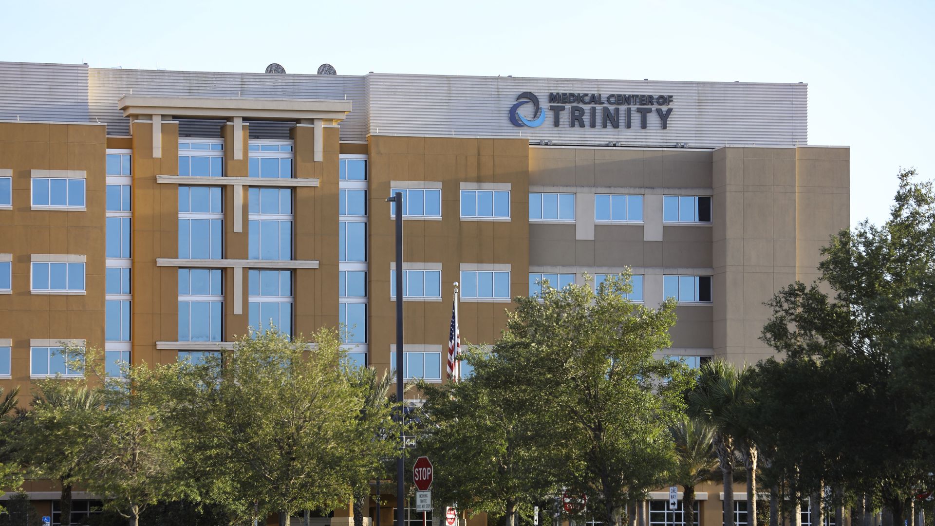 A beige hospital with the sign "Medical Center of Trinity" on top, and trees in the foreground.
