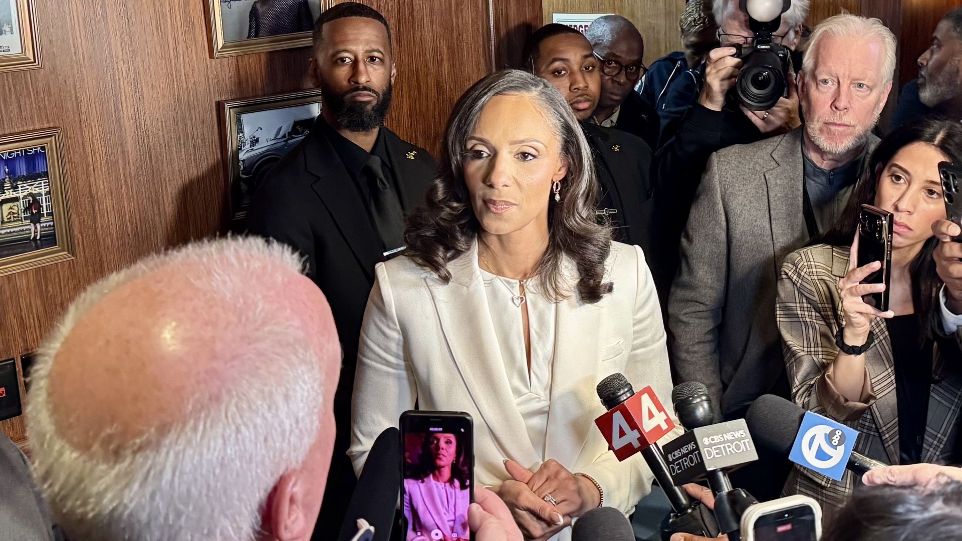 Sheffield in a white suit speaks with a crowd of reporters. 