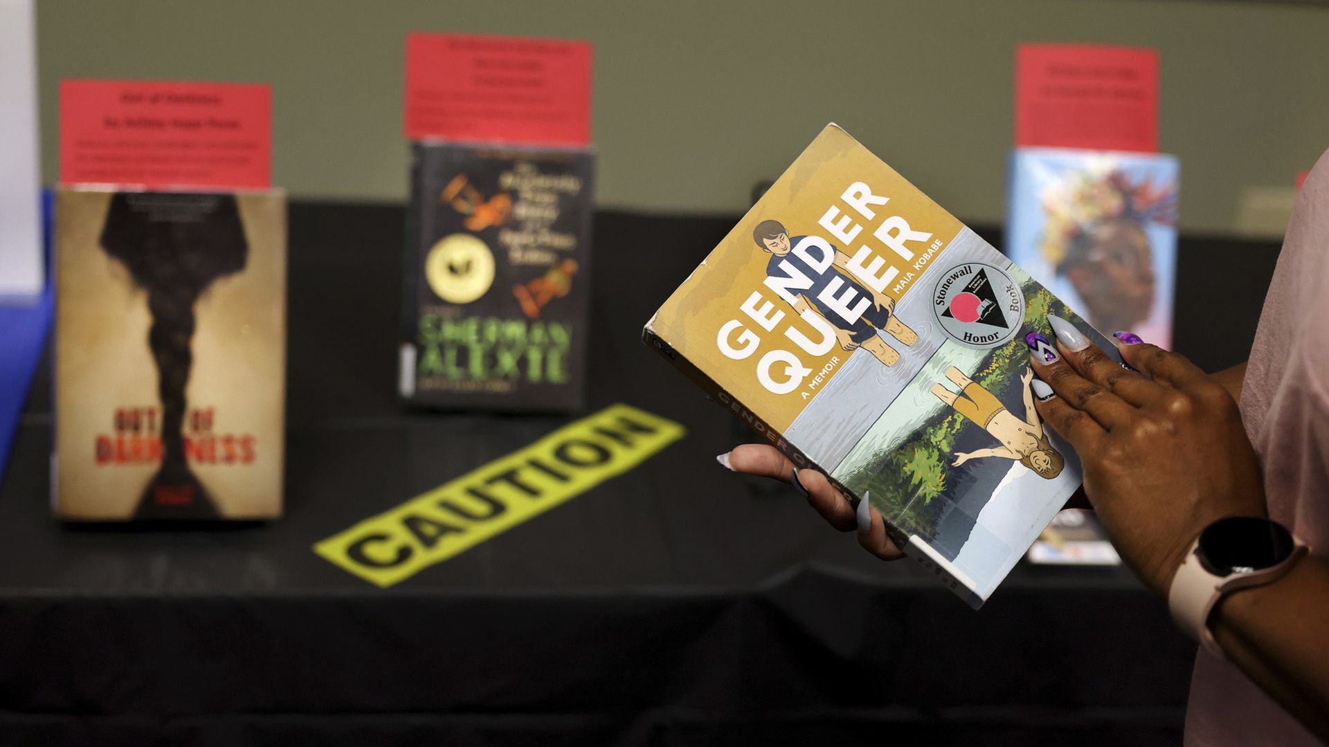 A person holding "Gender Queer: A Memoir" by Maia Kobabe in front of a banned book section at a Chicago library in September 2022.