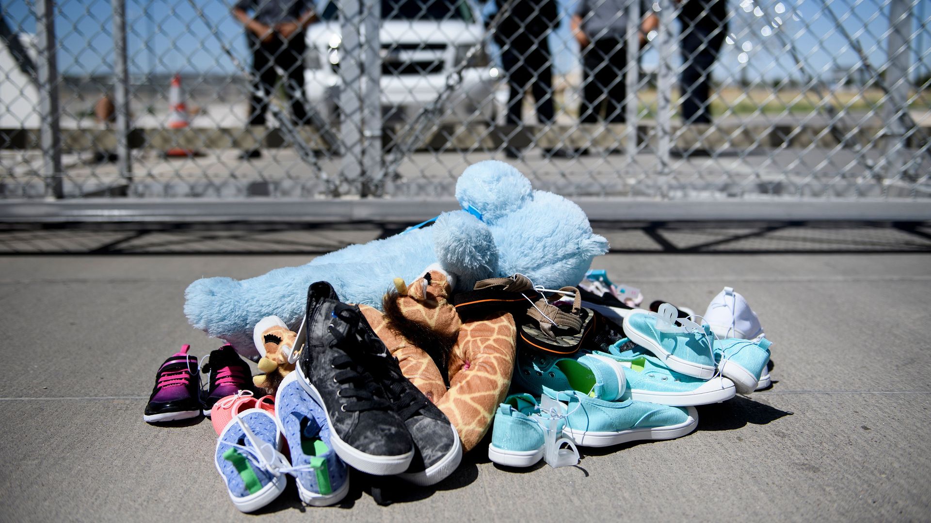 A pile of toys and small shoes in front of a chain link fence near the border. 