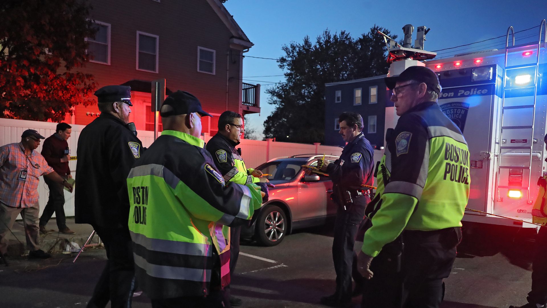 A group of officers, some in black and yellow jackets, gather outside a crime scene. 