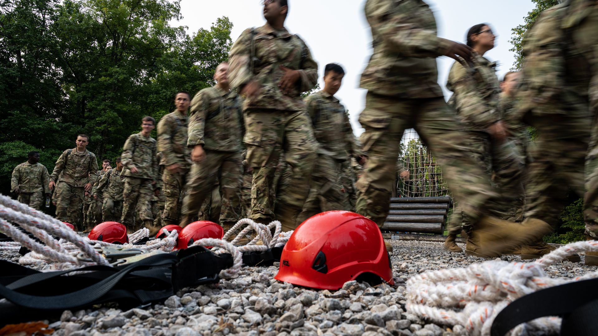 Photo of cadets walking in formation past safety equipment, including rope and a hard hat), in an outdoor camp