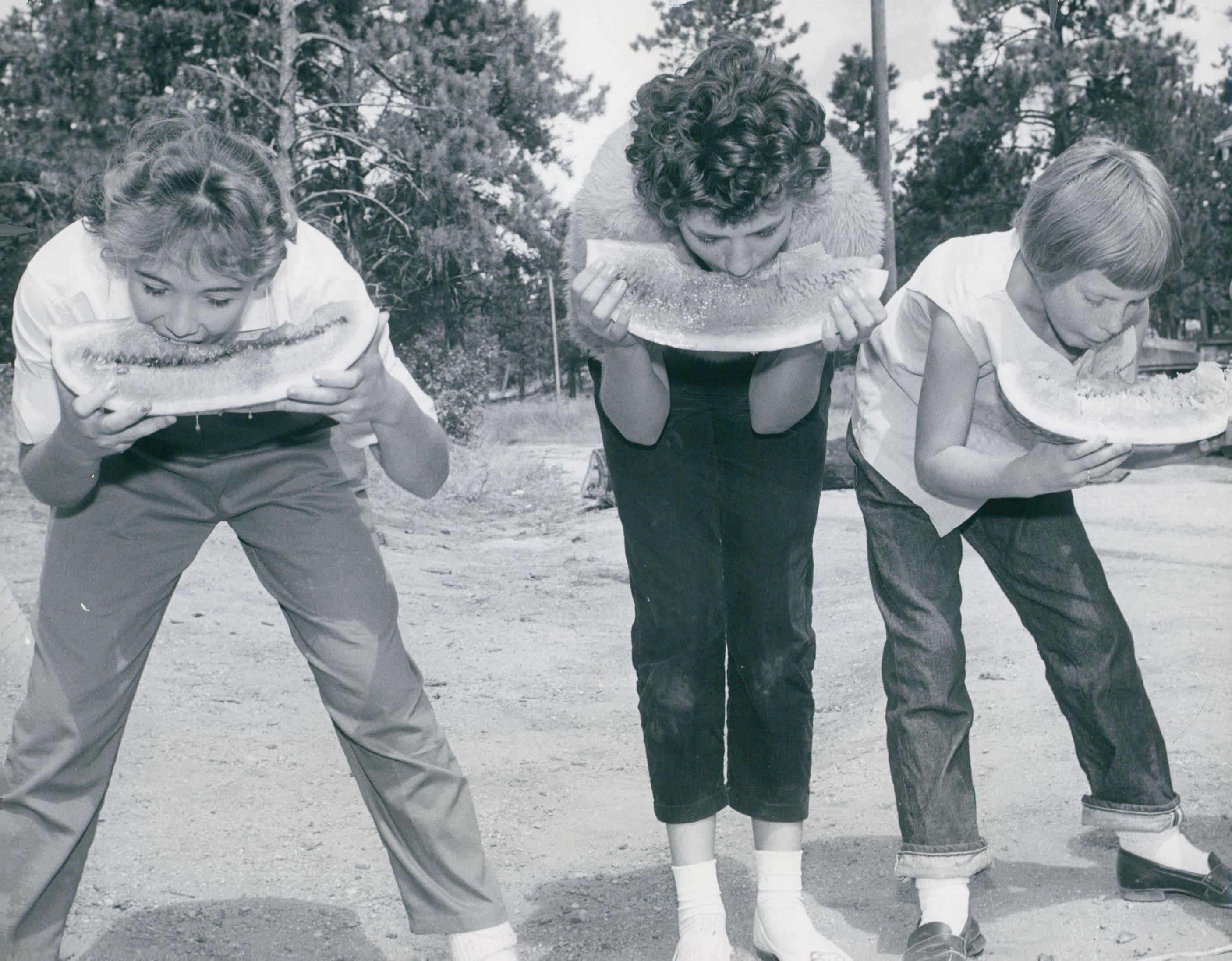 A black-and-white photo of three girls bent over biting into watermelon.