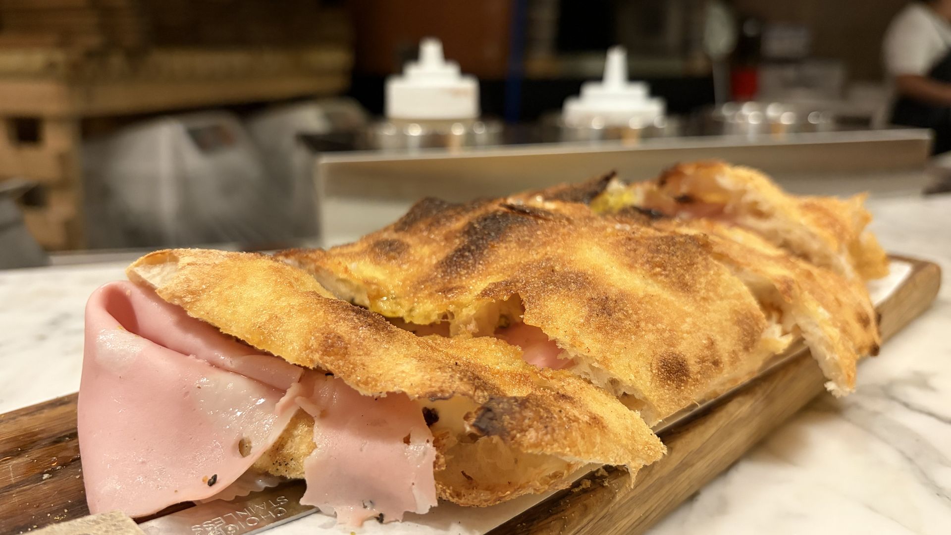 Close-up of a crusty saltimbocco sandwich held over a wooden board