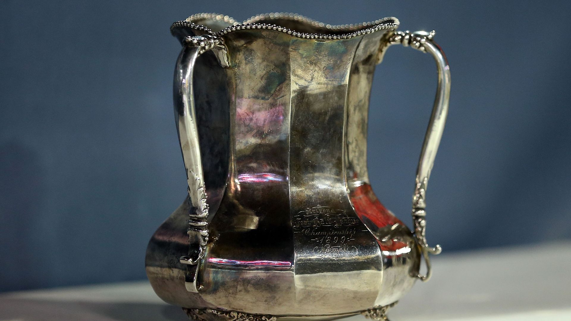 The Territorial Cup trophy, a silver colored metal jug that narrows above the bowl, with slim handles running along the side. 
