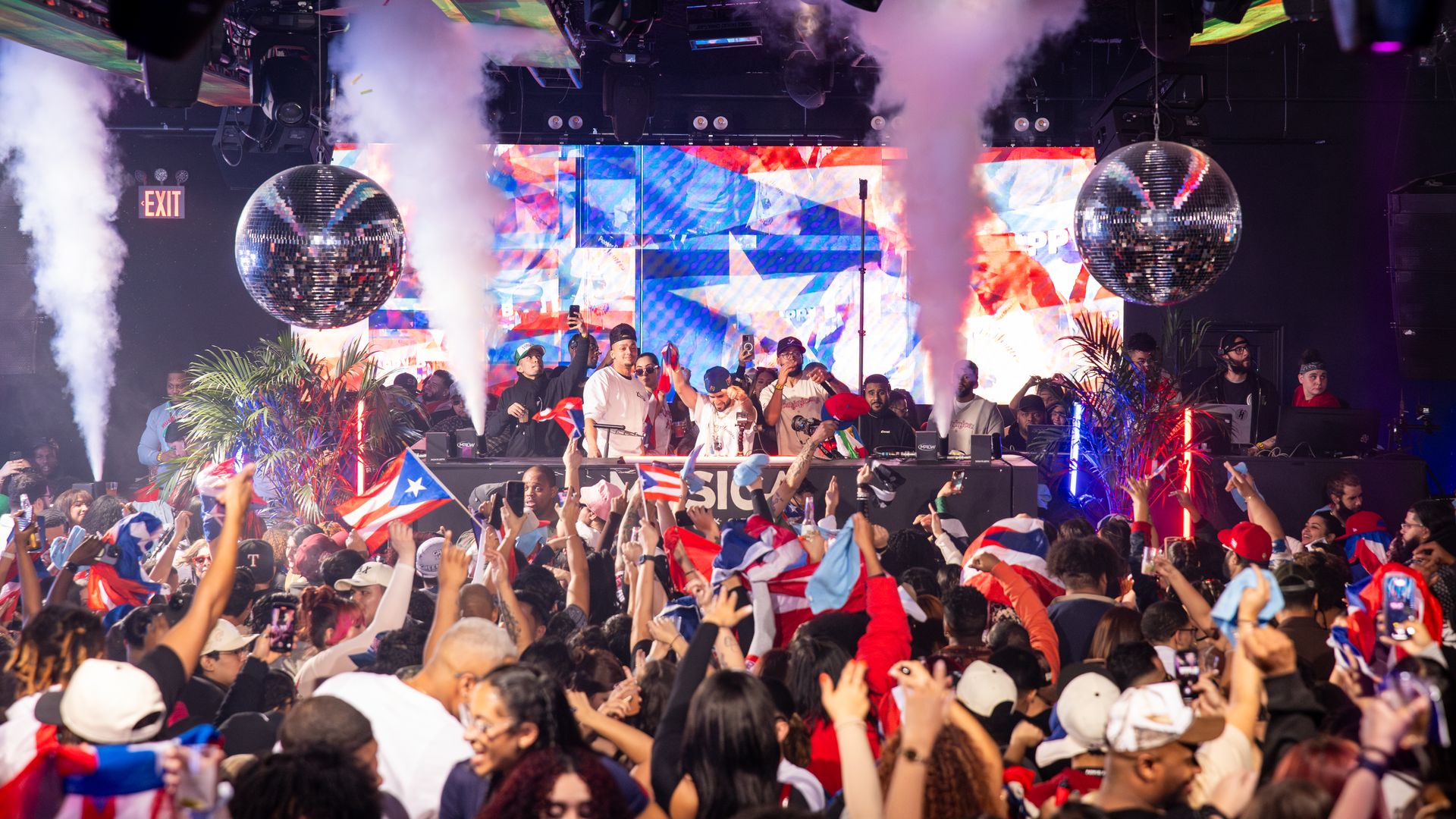 A crowd of people wearing Puerto Rican-themed clothes and waiving PR flags party at a 9am Banger party.