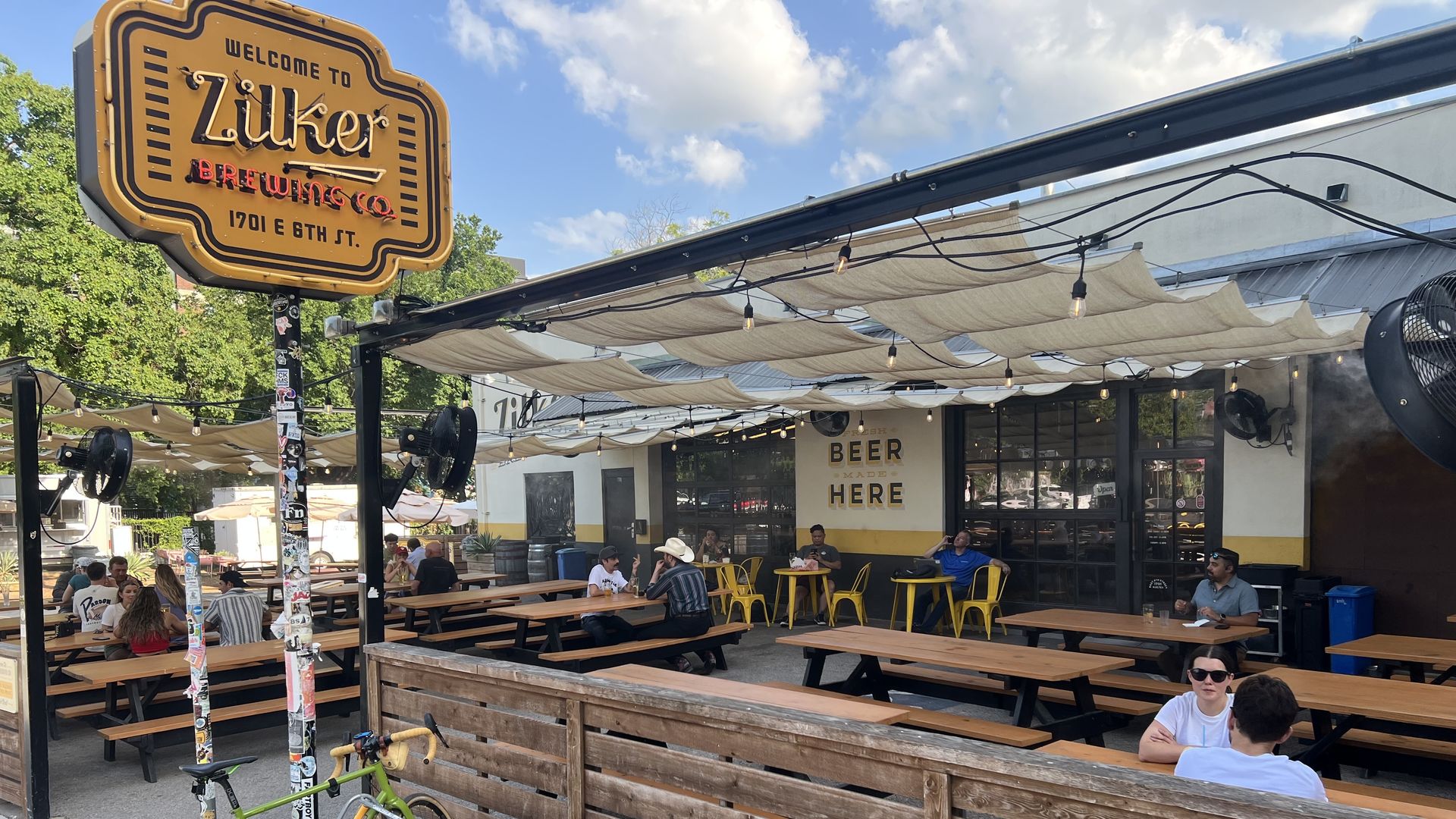 The outside of Zilker Brewery patio is shown with a few people sitting at wooden picnic tables