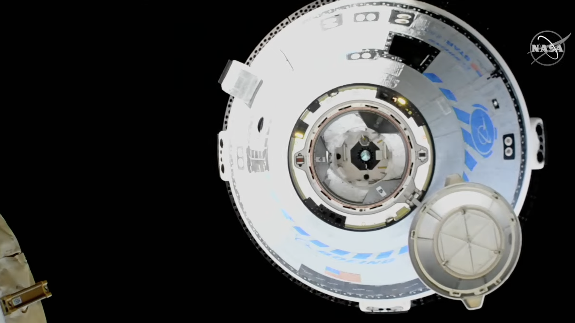 A full view of the Boeing Starliner capsule shining in white and blue against the blackness of space on approach to the ISS