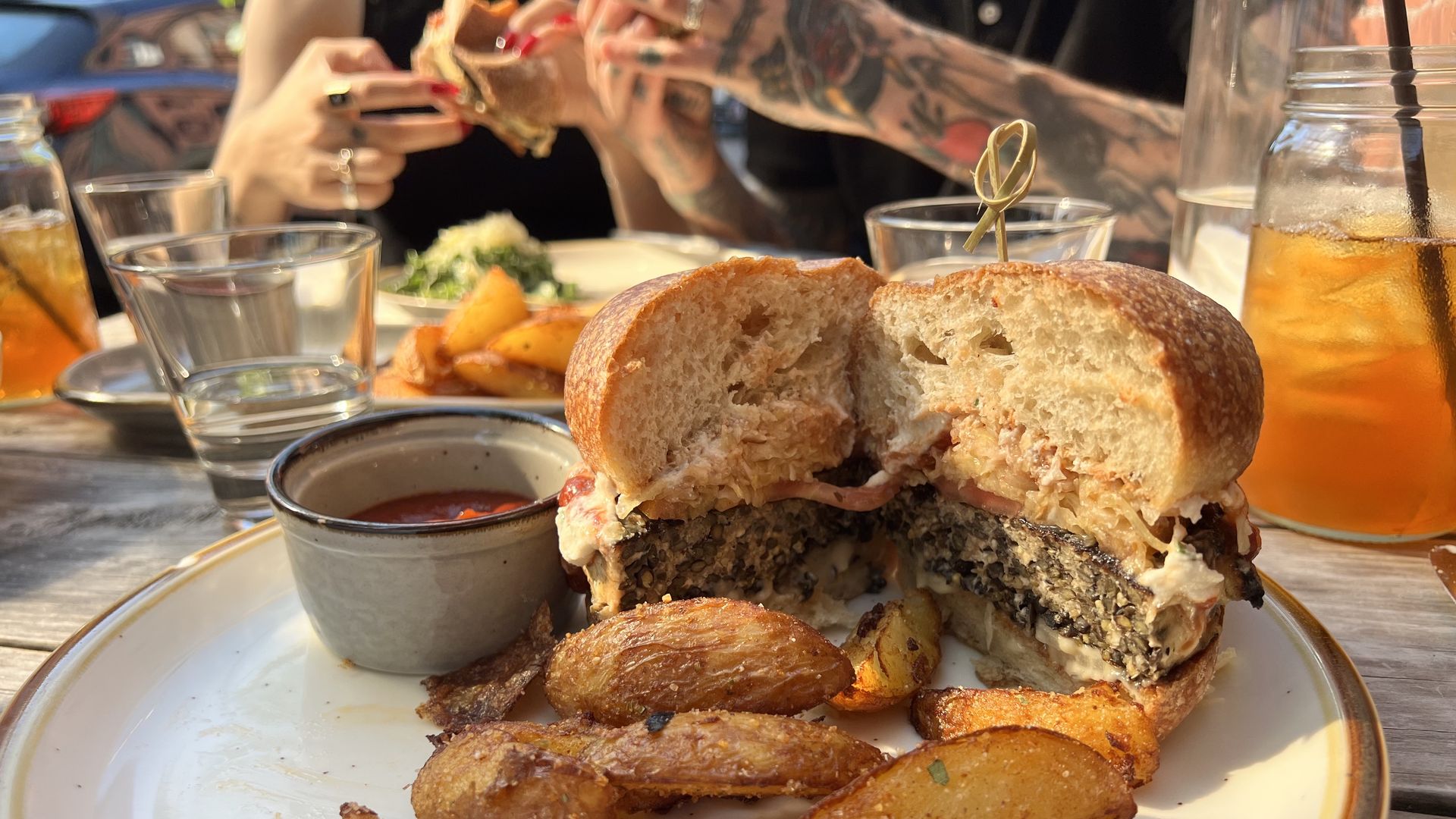 A photo of a burger cut in half on a plate with potato wedges.