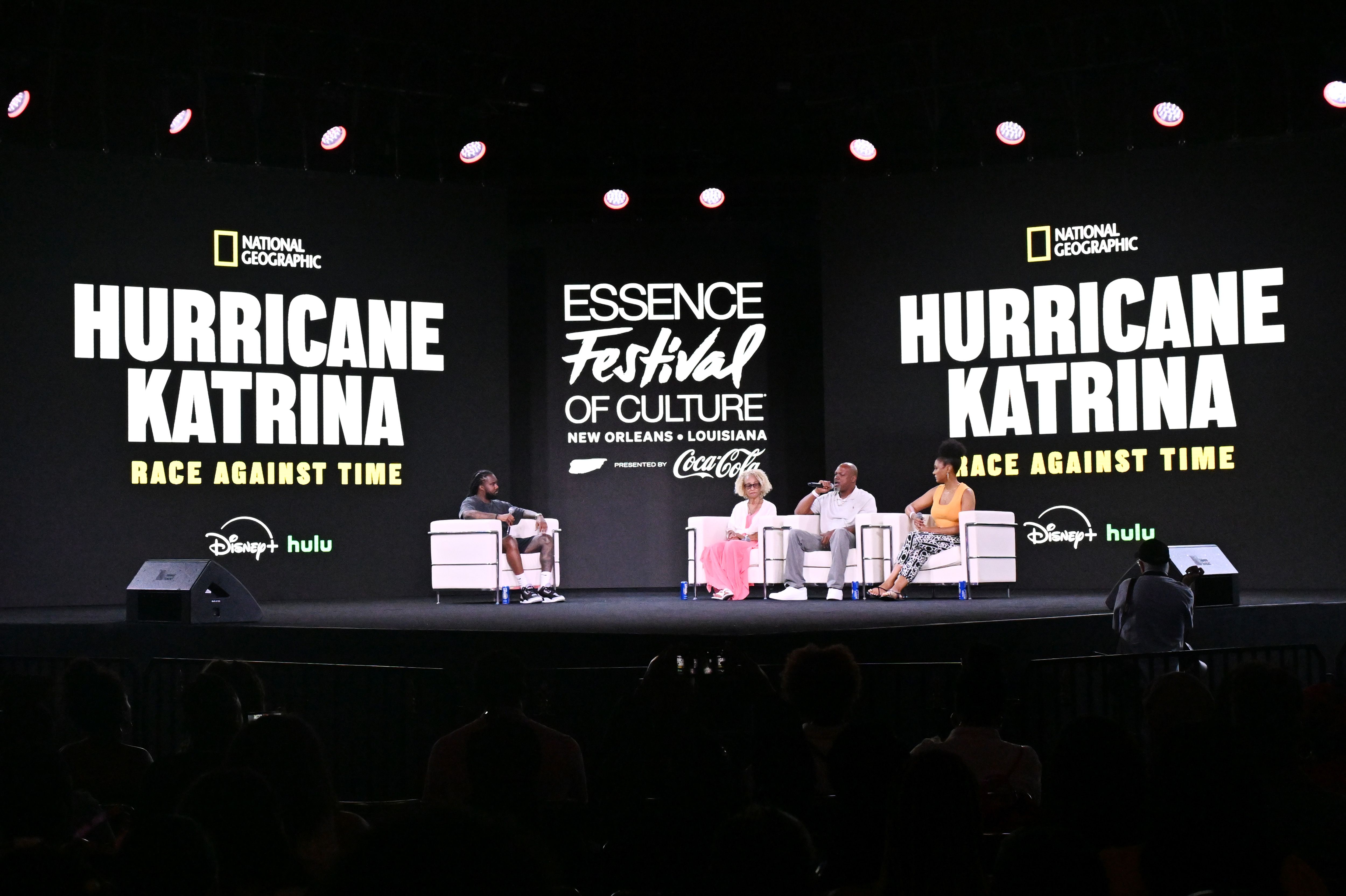 Panel discussion at the Essence Festival of Culture in New Orleans with large screens displaying National Geographic’s "Hurricane Katrina: Race Against Time" and Disney+ Hulu logos.