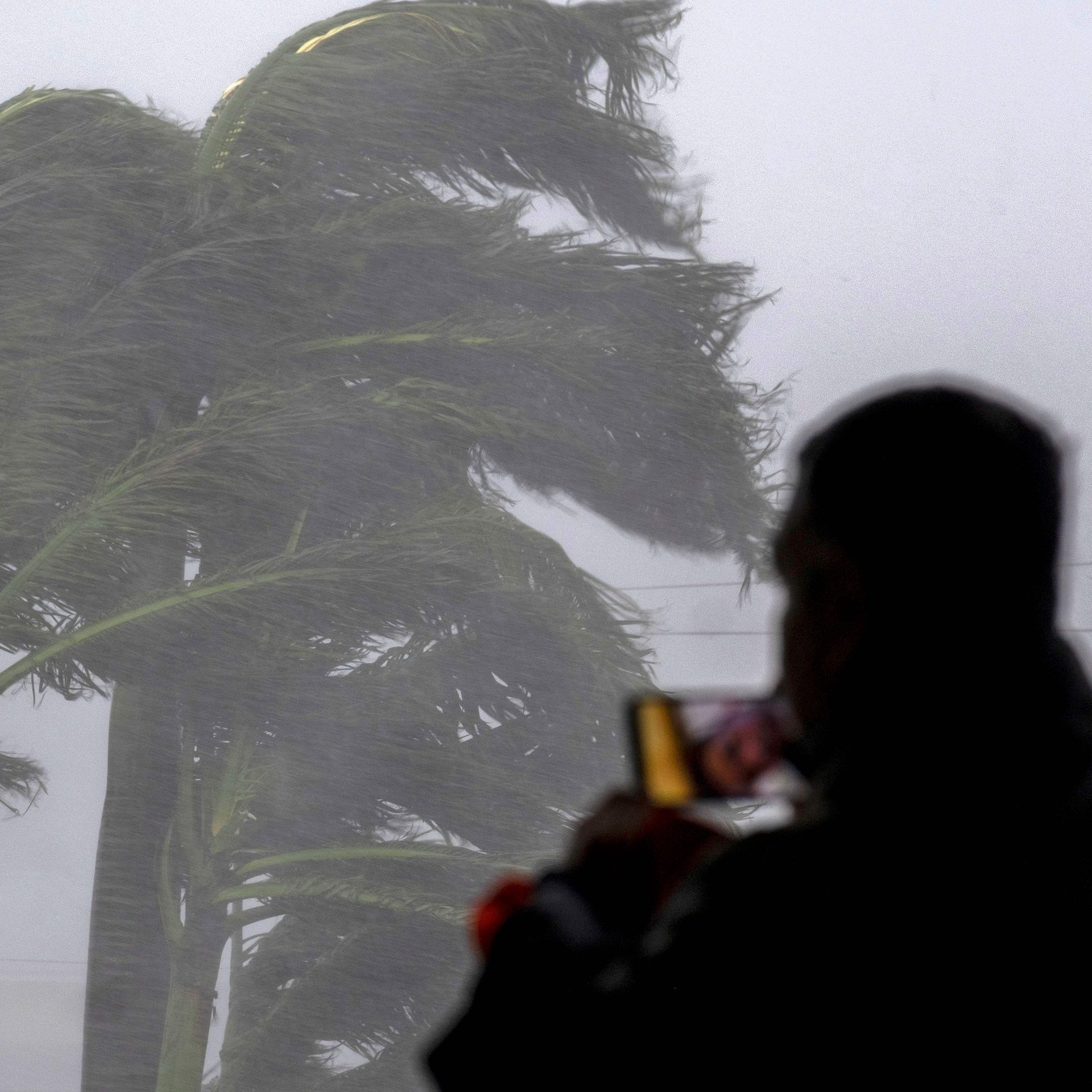 The silhouette of a person films Hurricane Ian outside on their phone.