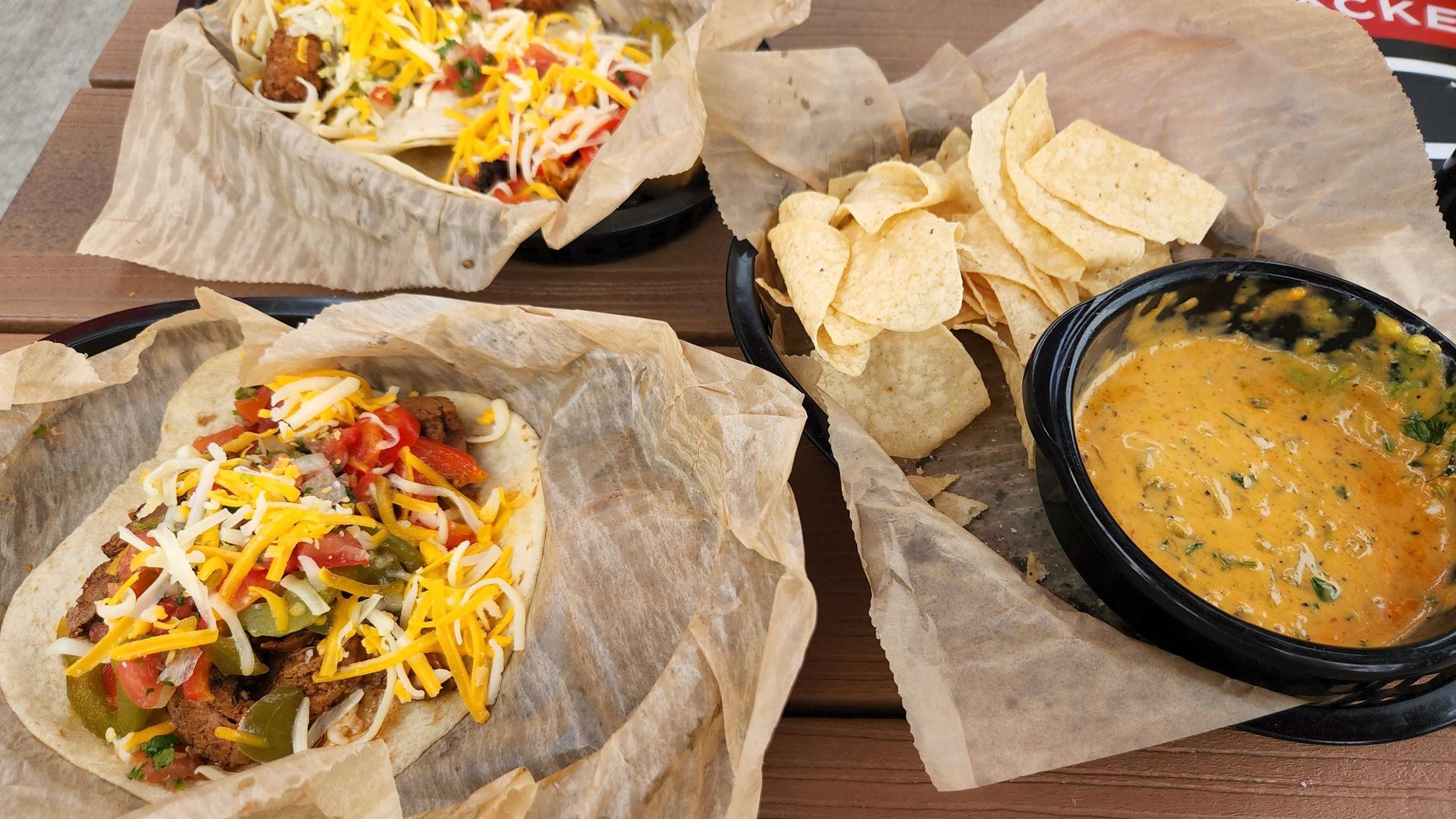 An overview of tacos and queso dip in brown paper-lined baskets