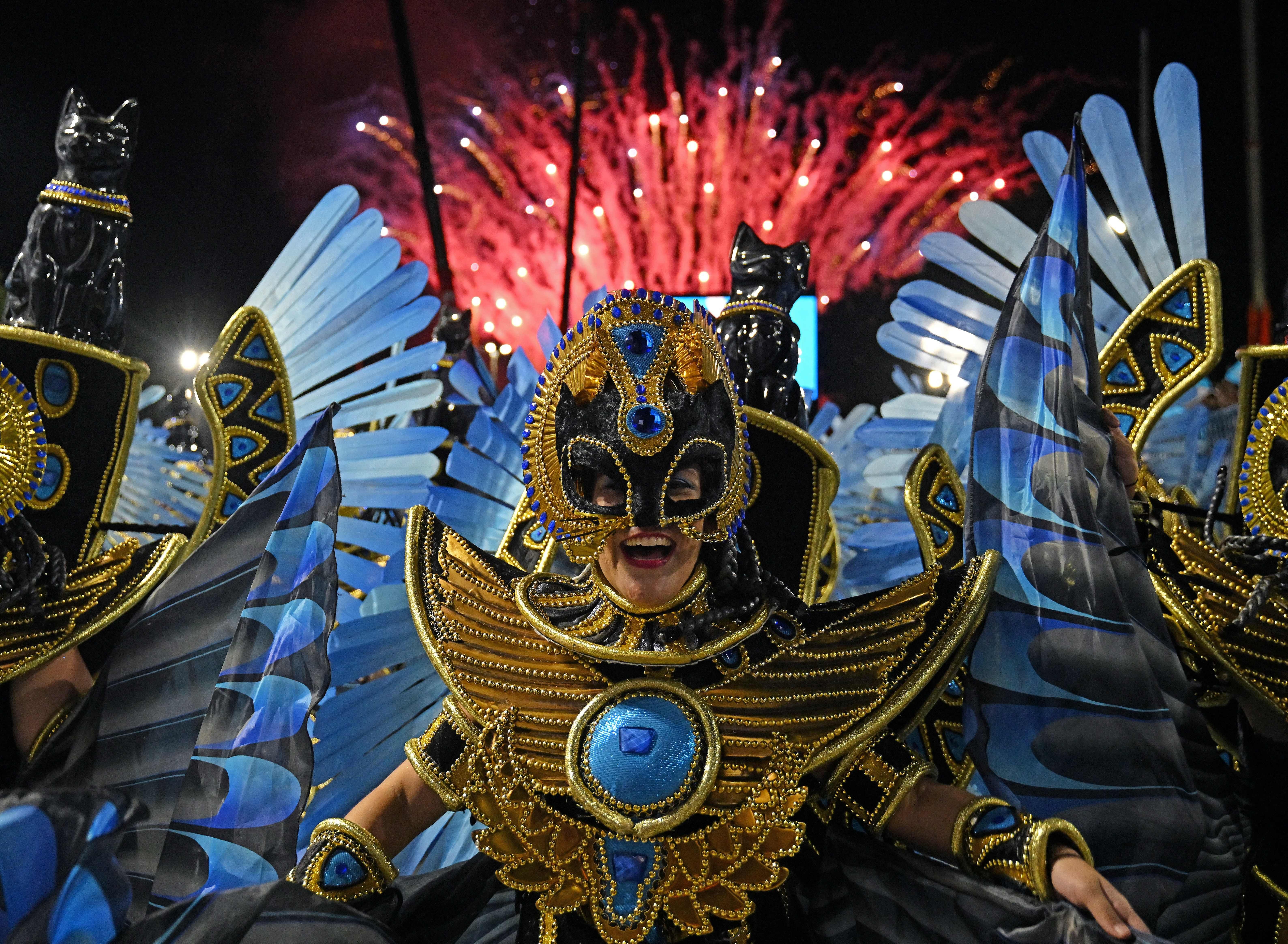 A woman smiles while dressed in an elaborate costume with gold and blue details and blue wings