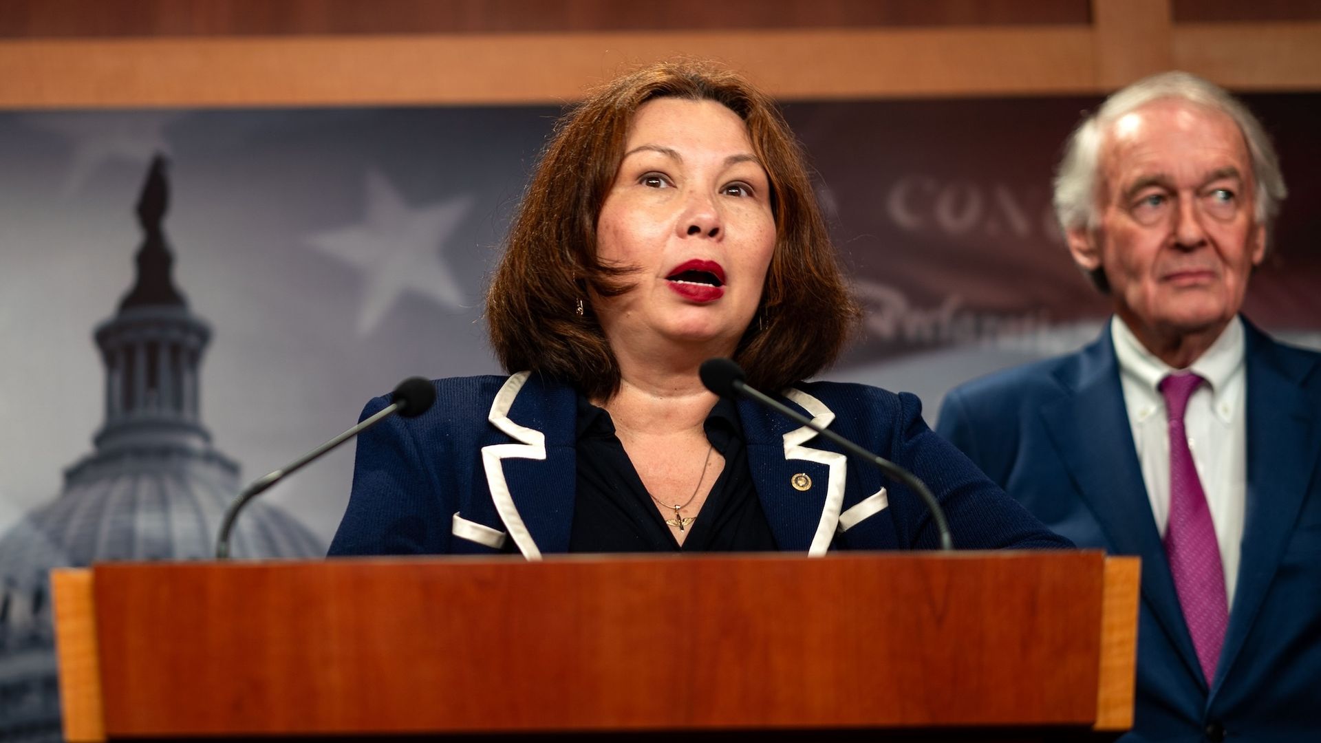 Photo of a woman on a podium talking to reporters