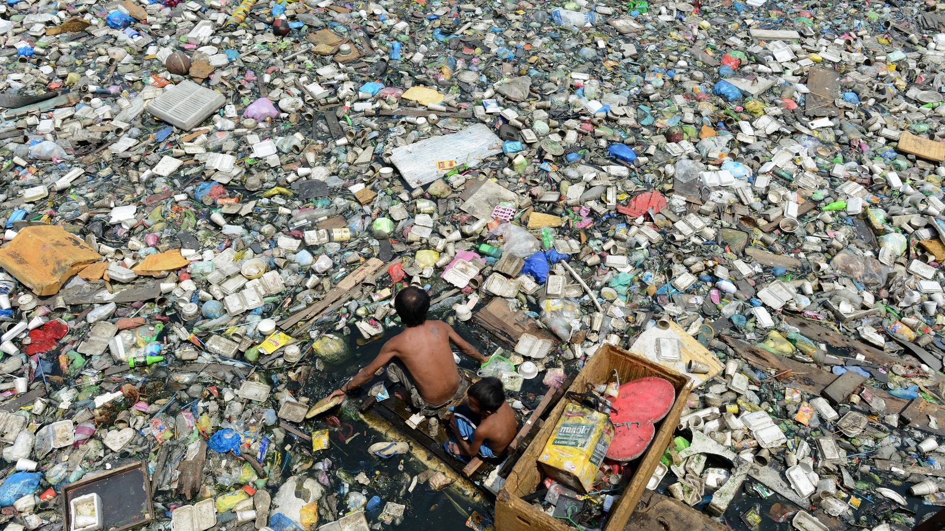 A father and son on a makeshift boat paddle through a garbage filled river as they collect plastic bottles that they can sell in junkshops in Manila.