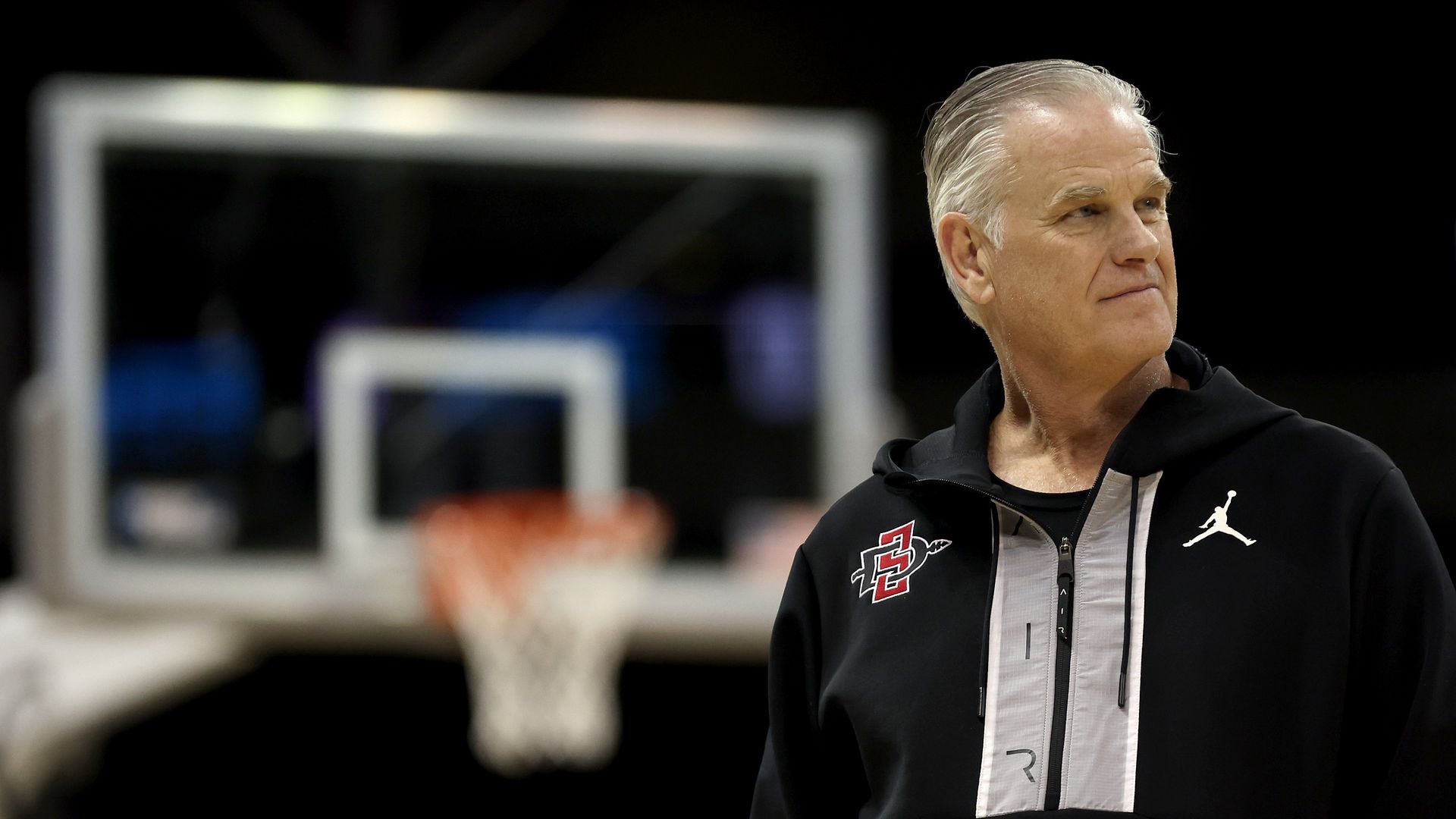 SDSU Aztecs basketball coach Brian Dutcher in front of an out-of-focus basketball hoop