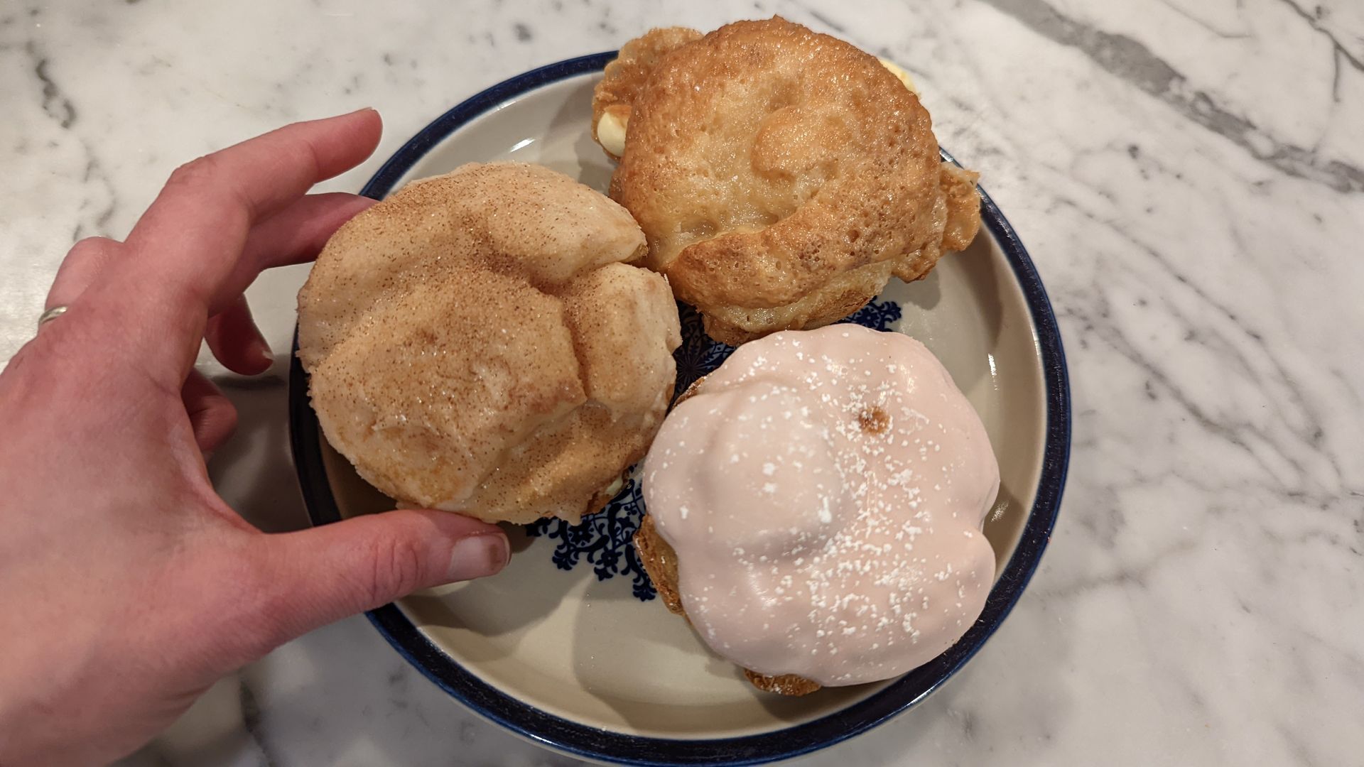 A person's hand holds a cream puff covered in cinnamon and sugar.