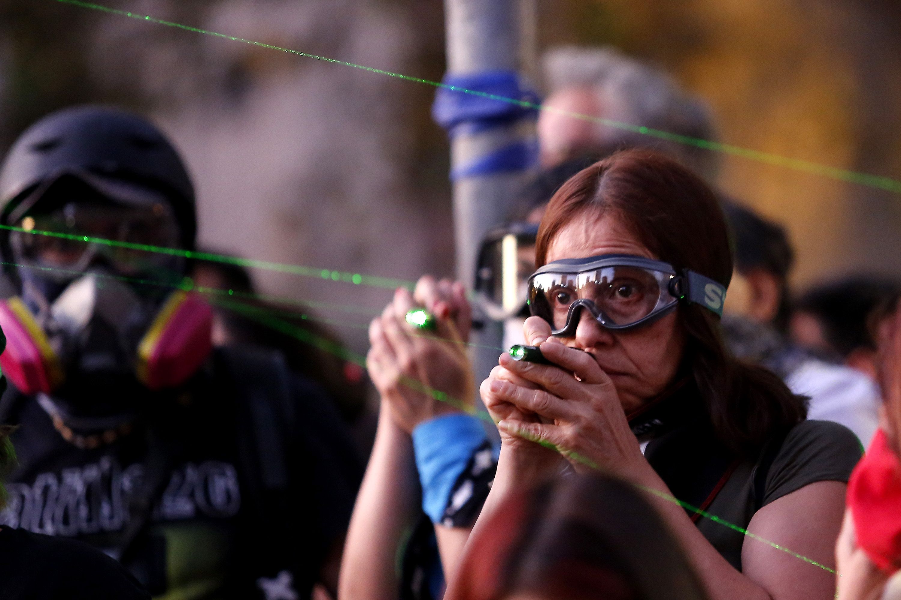 In this image, a woman points a laser at police while wearing safety goggles