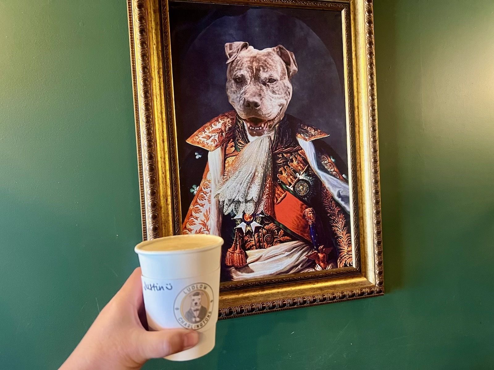 Photo of a coffee cup in front of a painting of a dog. 