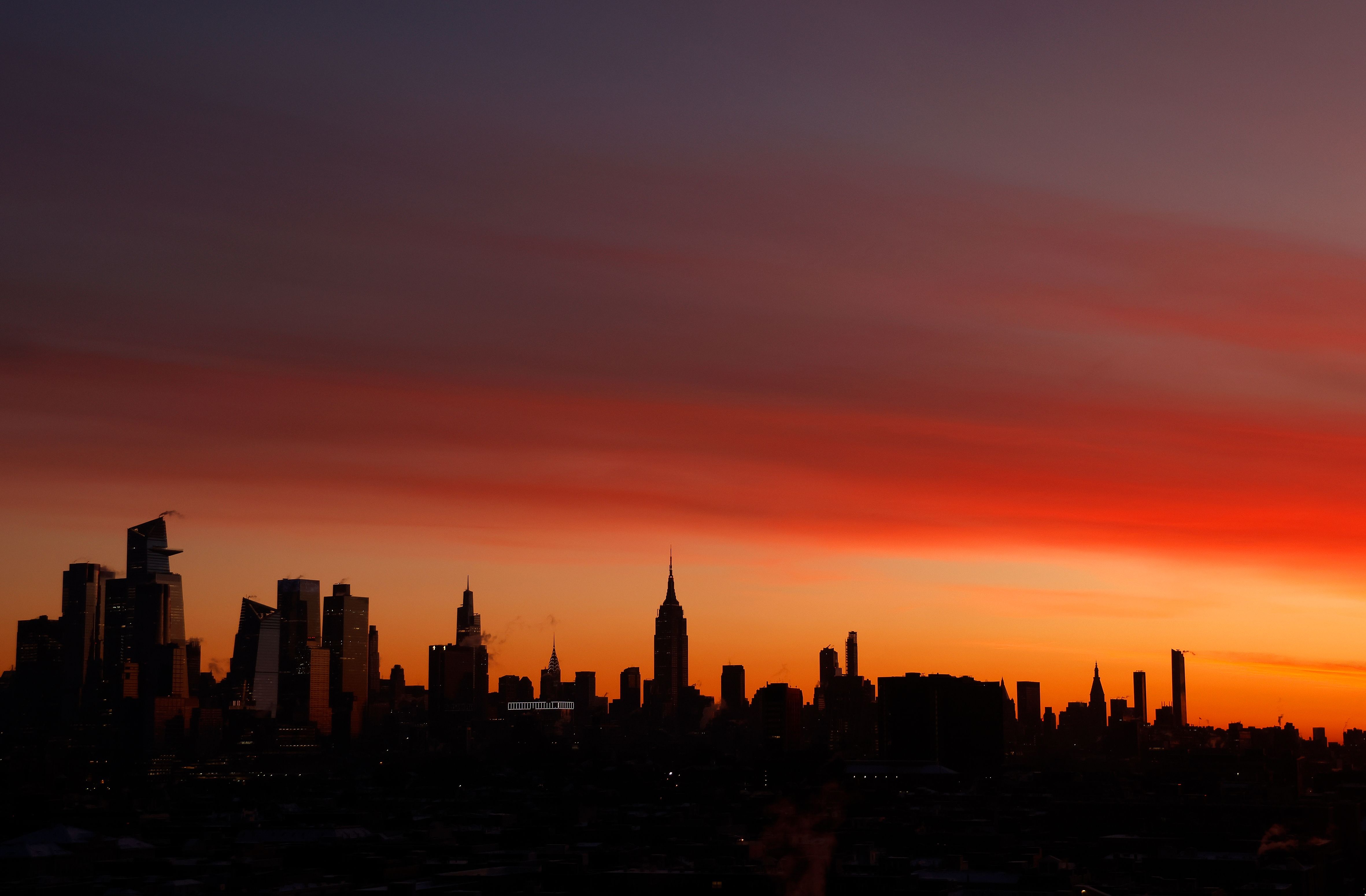 Manhattan's skyline silhouetted against an orange and purple sunrise