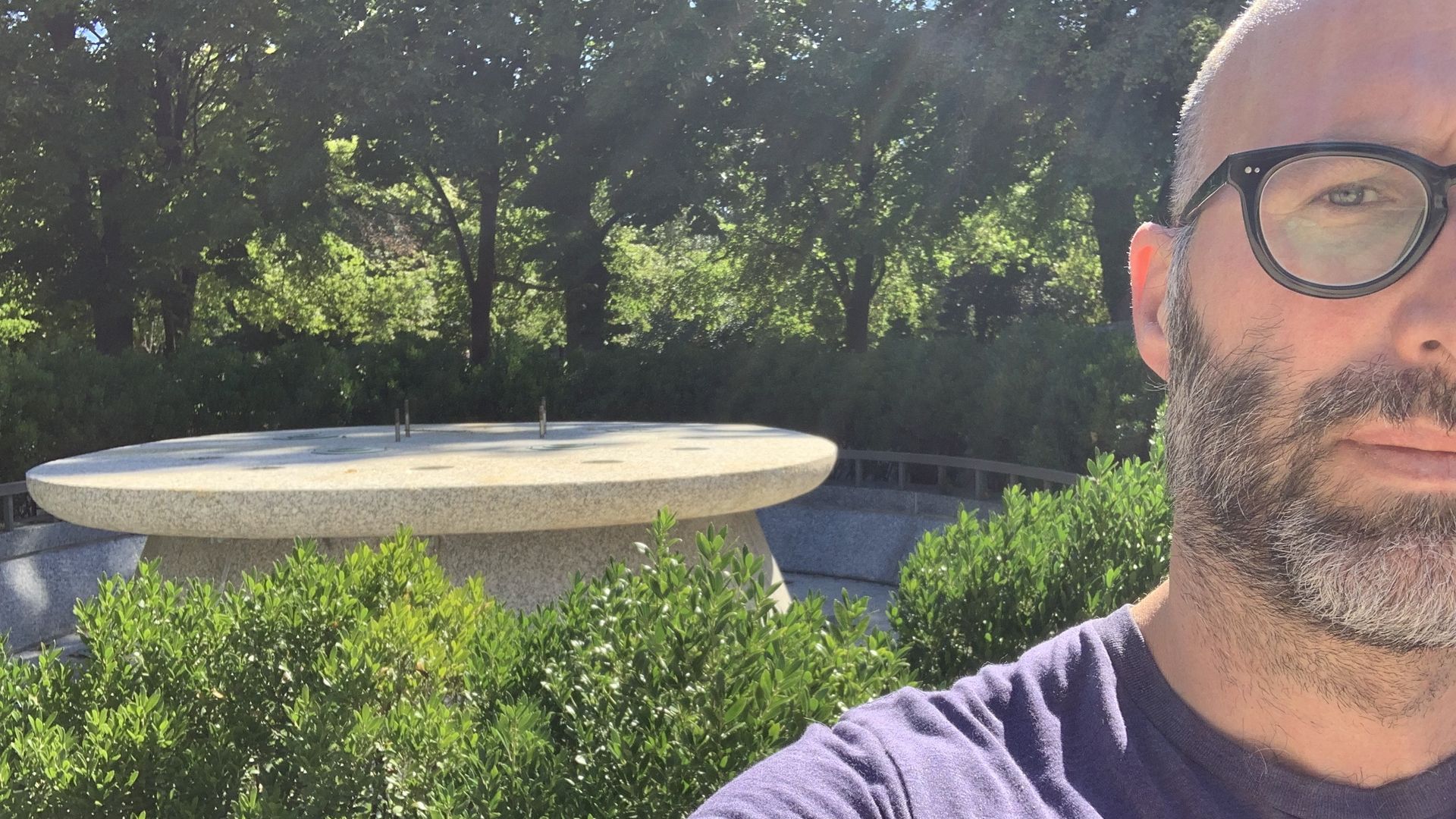 Photo of a man posing in front of an empty pedestal in a park