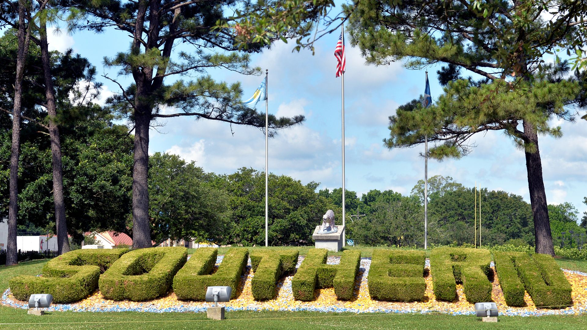 An American flag is seen behind green boxwoods that are cut to spell out "SOUTHERN."