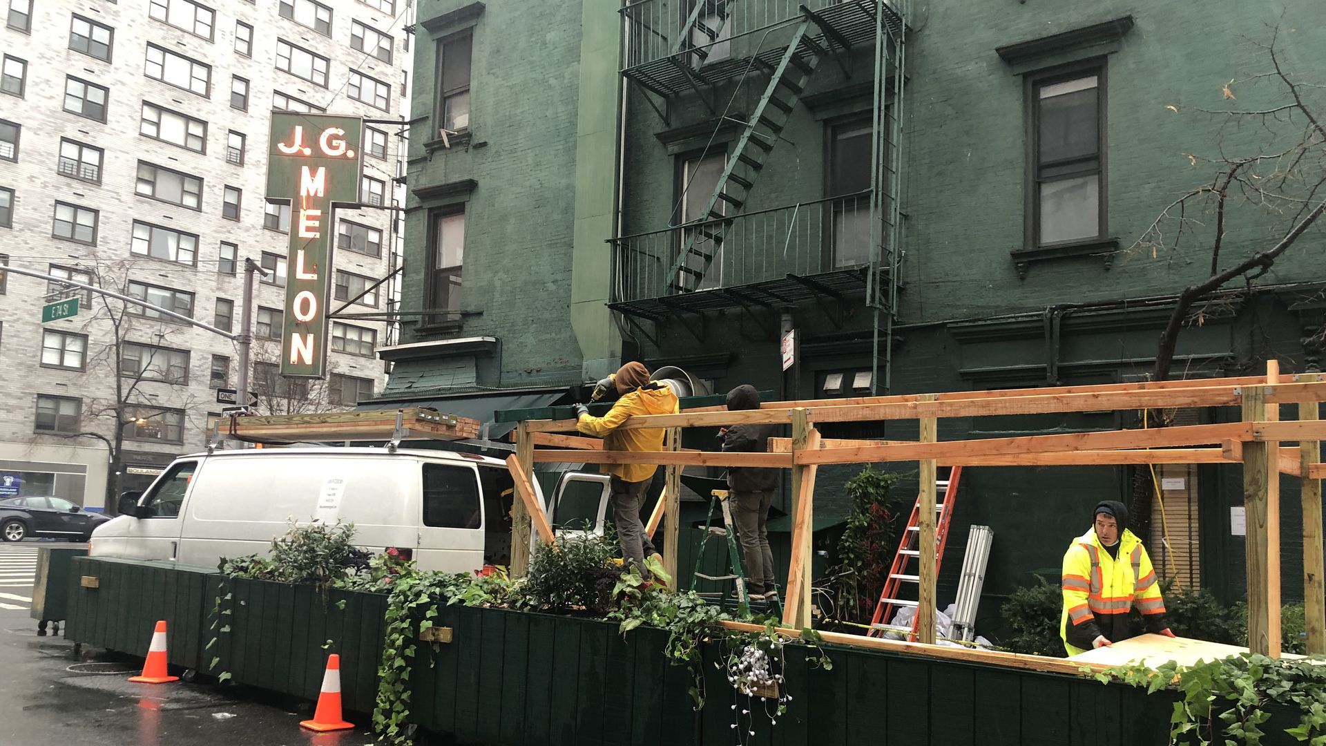 Photo of workers dismantling wooden structure for outdoor seating next to a building