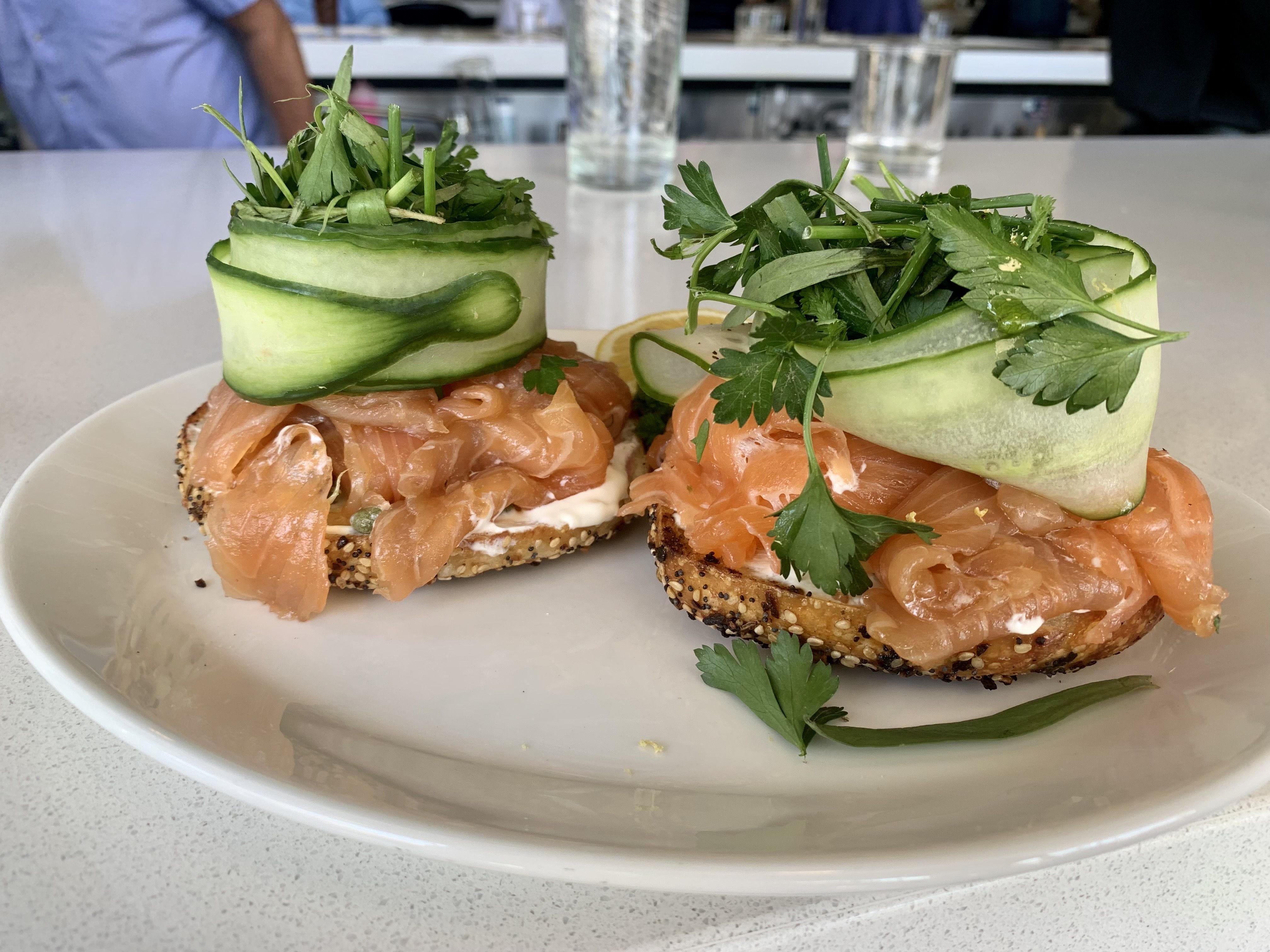 a tall stack of smoke salmon on a bagel topped with cucumber