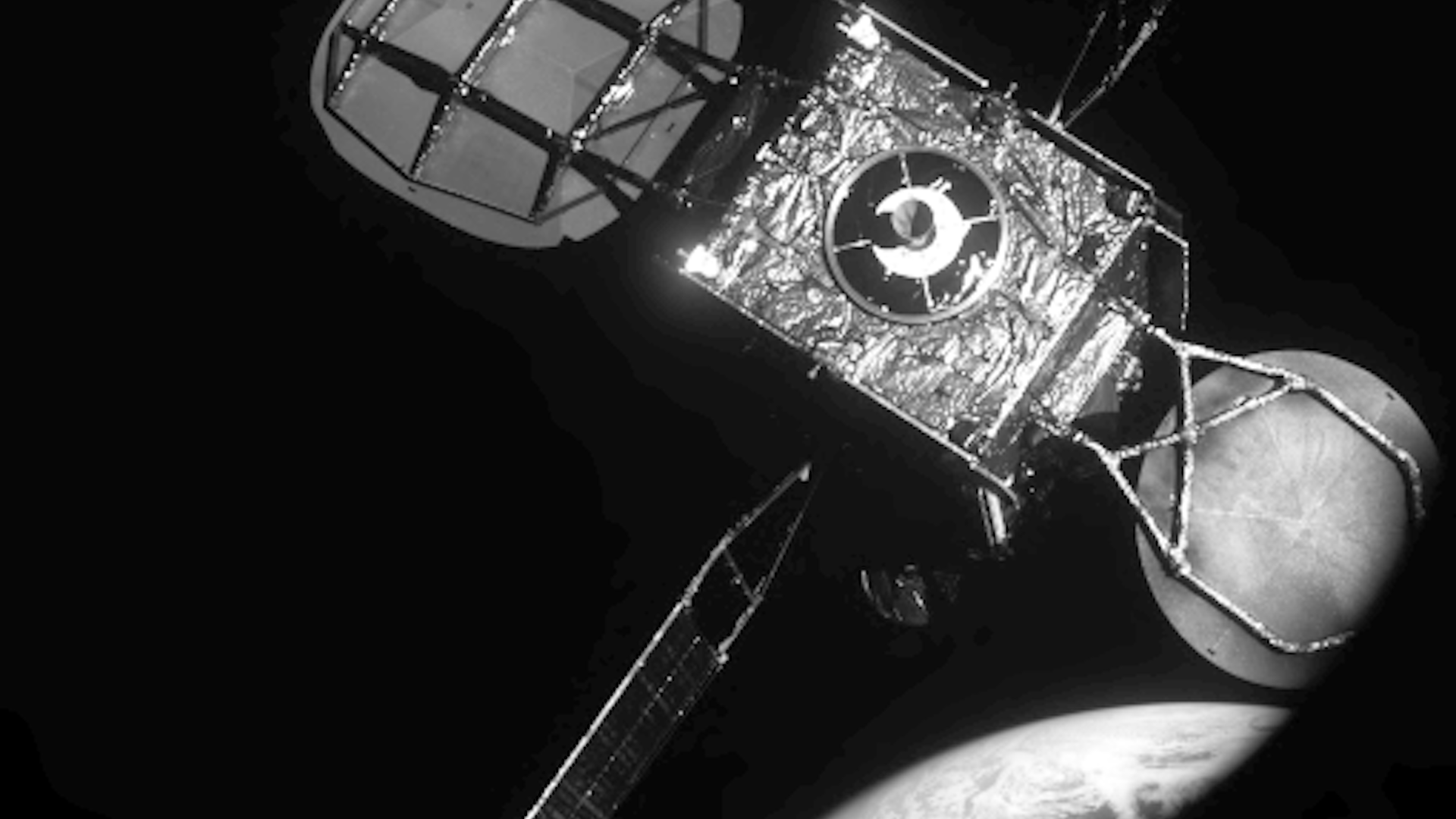 A satellite comes into view above Earth in black and white as seen by another satellite