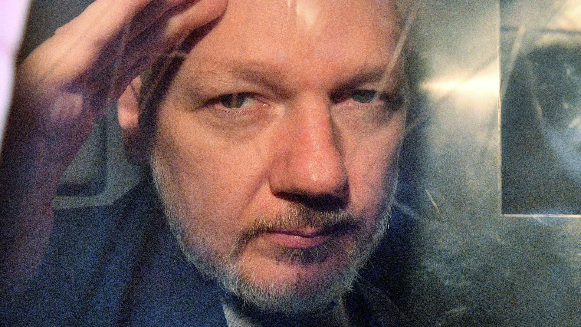 Photo of Julian Assange's face peering through a prison van window