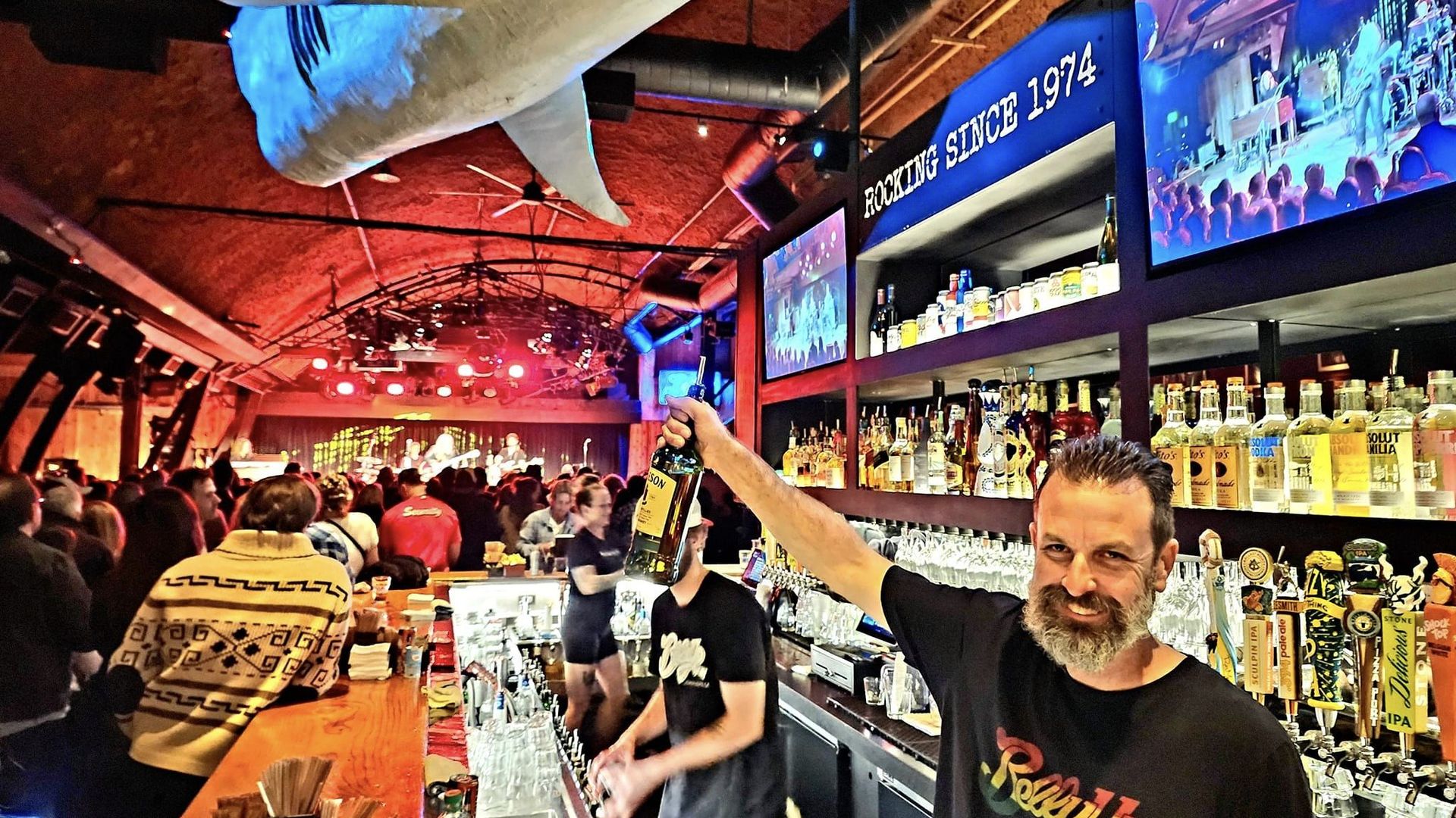A bartender holds up a bottle of alcohol in front of a big crowd of people during a concert.