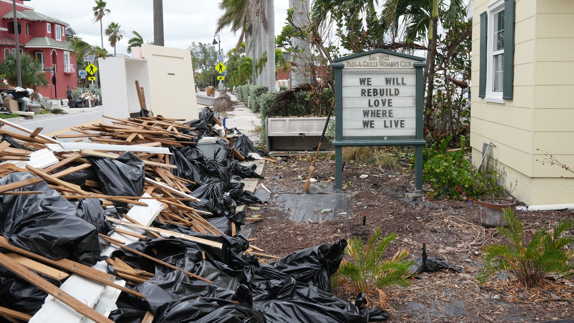 A pile of trashbags and construction debris next to a sign for the Pass-A-Grille Woman's Club that reads, "WE WILL REBUILD LOVE WHERE WE LIVE."