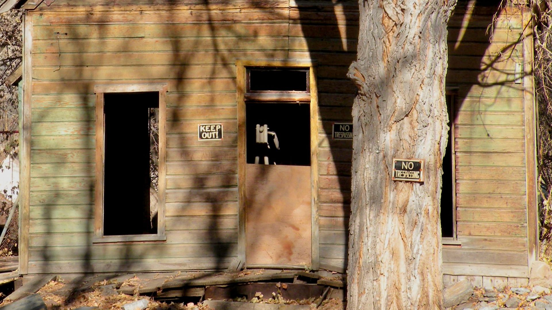 Signs reading "No trespassing" and "Keep out" decorate a decaying wood house.