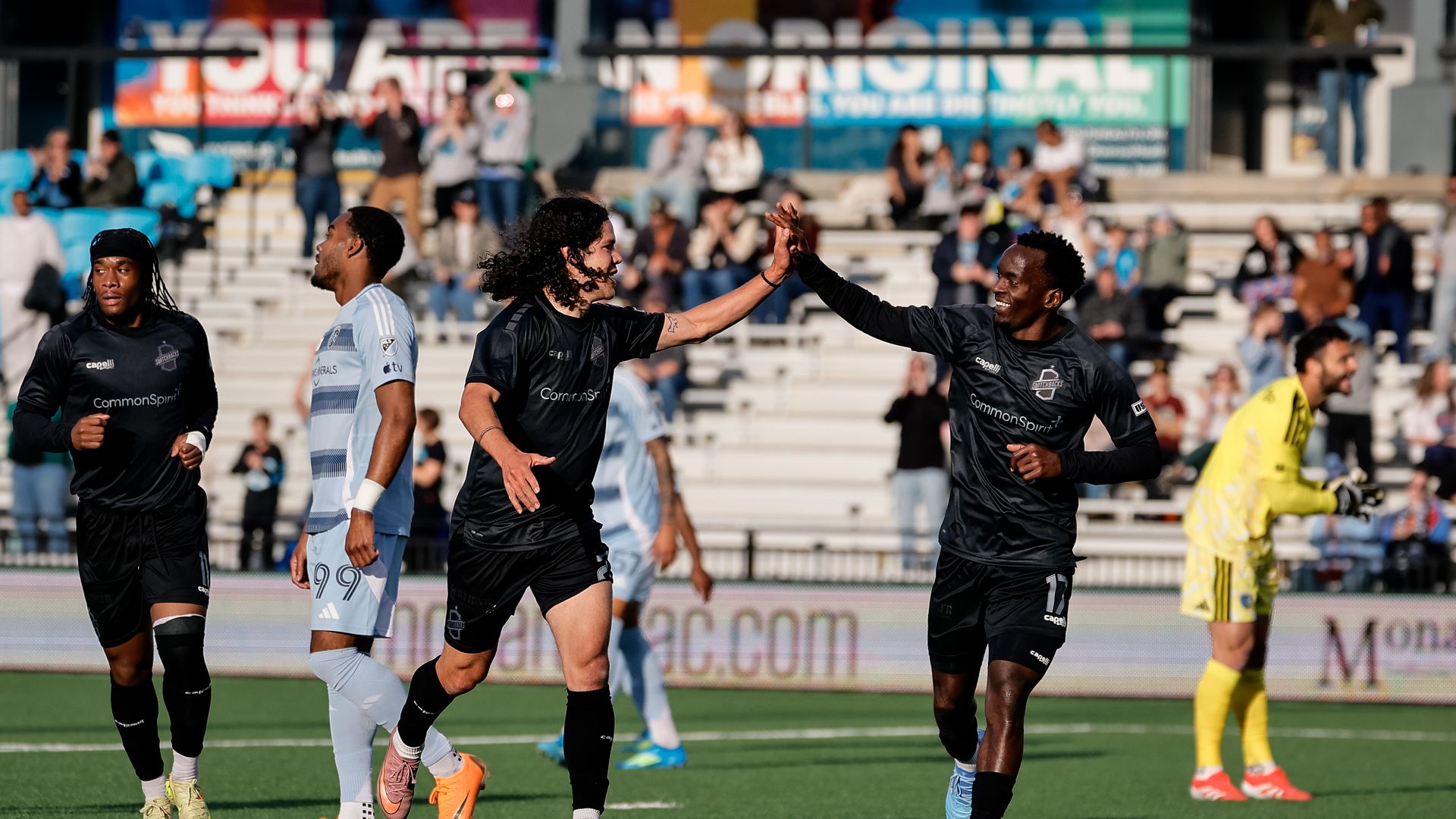 Two soccer players in black jerseys exchange a high-five while smiling. 