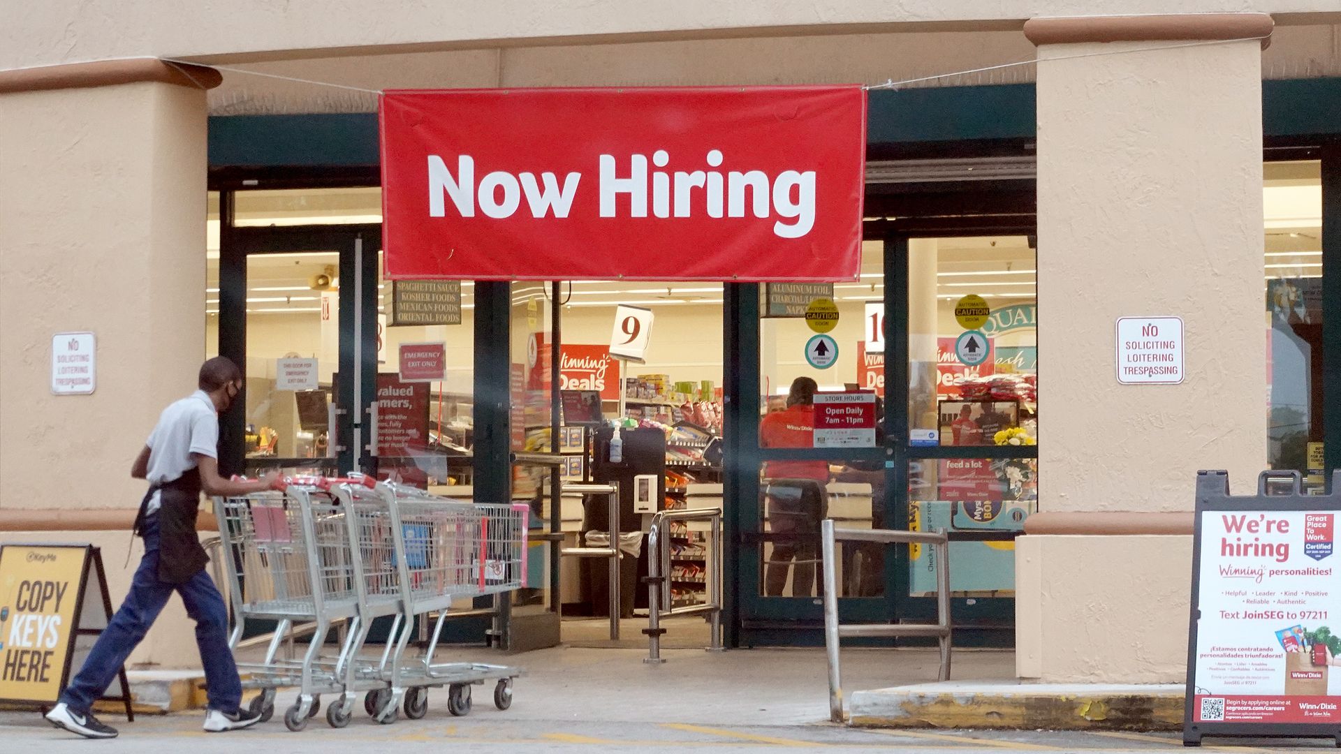 Worker pushing carts with a now hiring sign