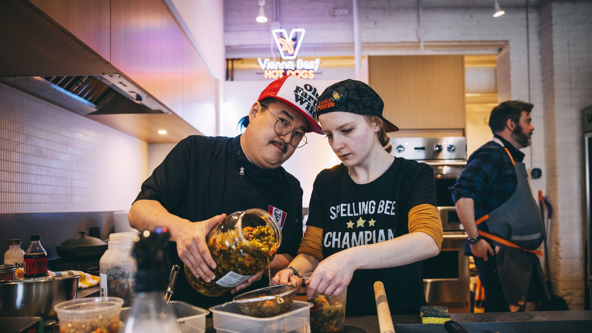 Dennis Lee in an industrial kitchen, emptying a massive jar of giardiniera into a strainer with his wife.
