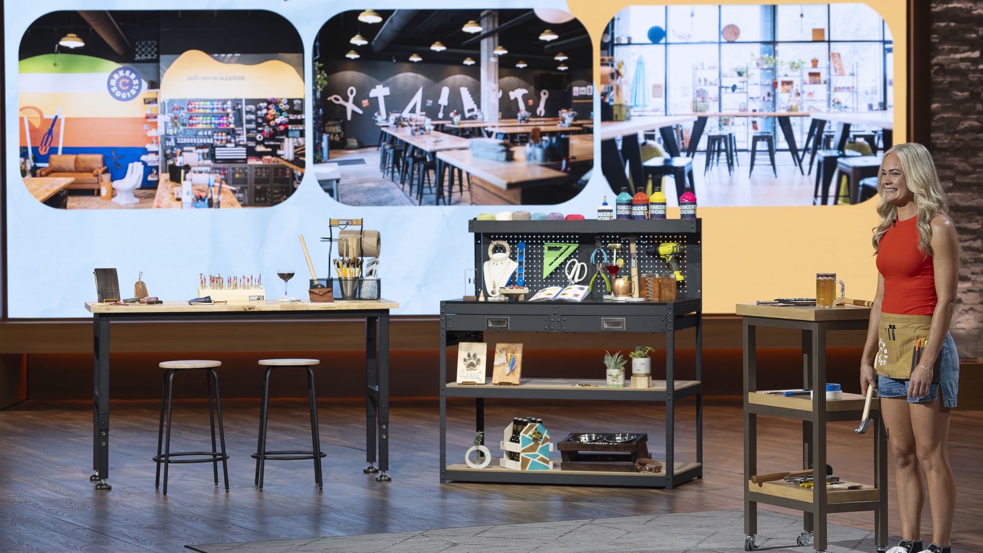 Megan Pando, in red top and denim shorts, stands next to work tables and tool displays on a stage with a large Makers Social logo screen showing workshop images in background.