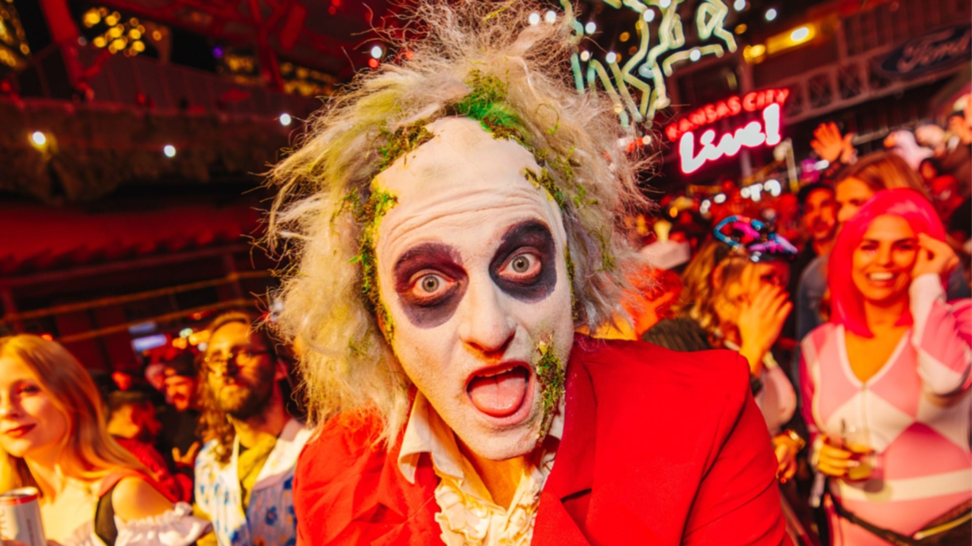 Person dressed as Beetlejuice with wild white hair, green moss, white face paint, dark eye circles, and red suit at a previous End of Days event at KC Live! in Power and Light.