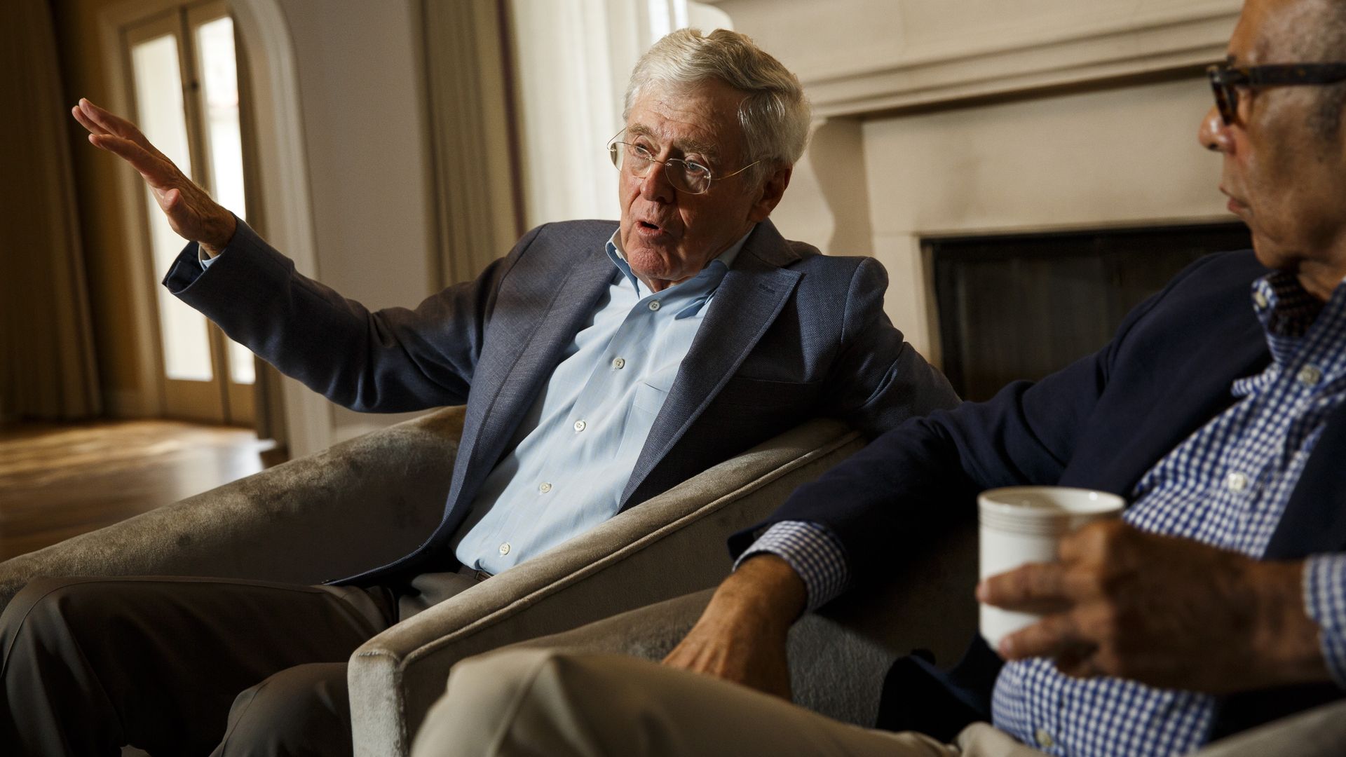 In this image, Charles Koch sits and gestures while talking.