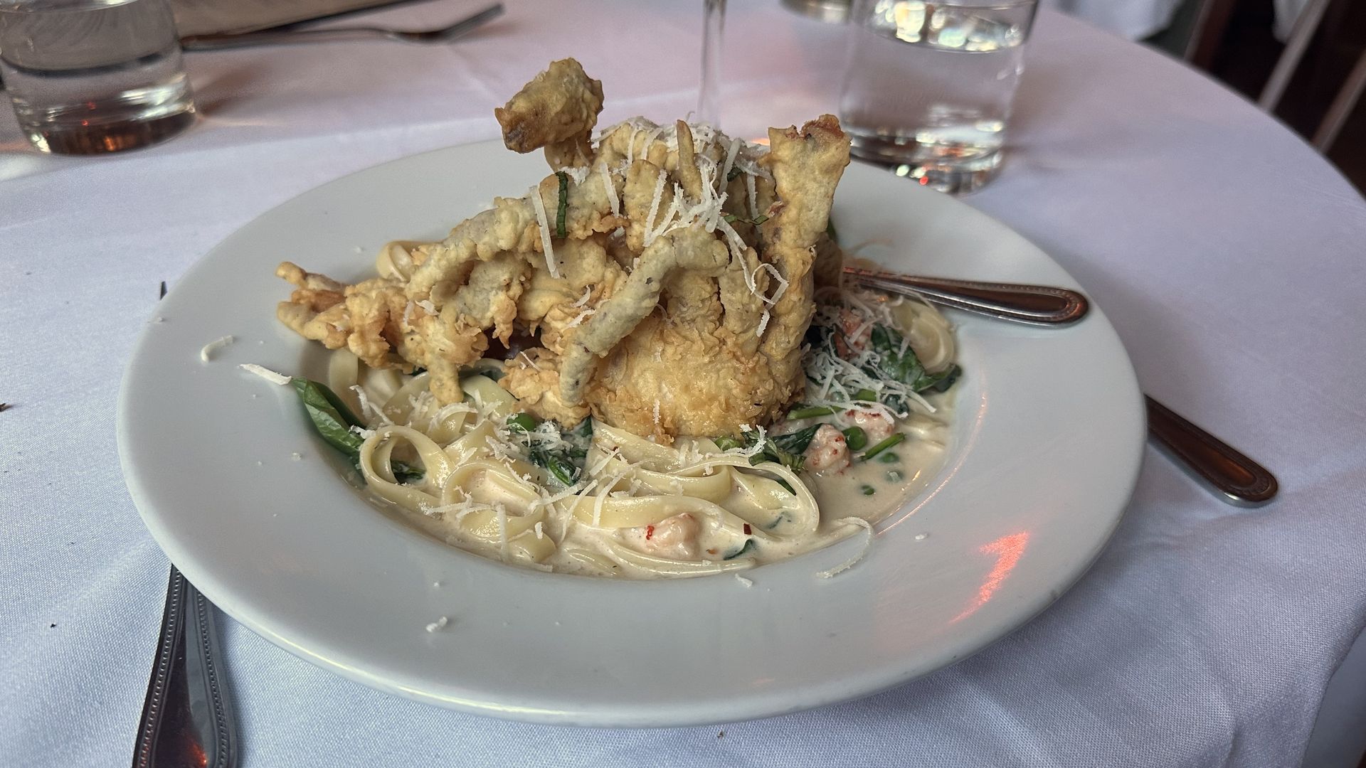 A large white pasta dish is filled with a fettuccine pasta and topped with a fried soft shell crab.