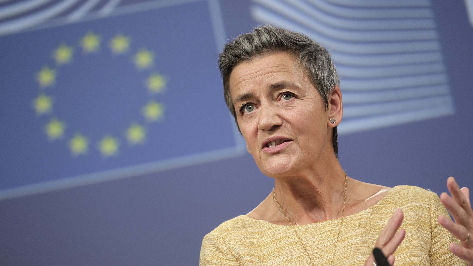 EU competition official Margrethe Vestager speaking in front of an EU flag