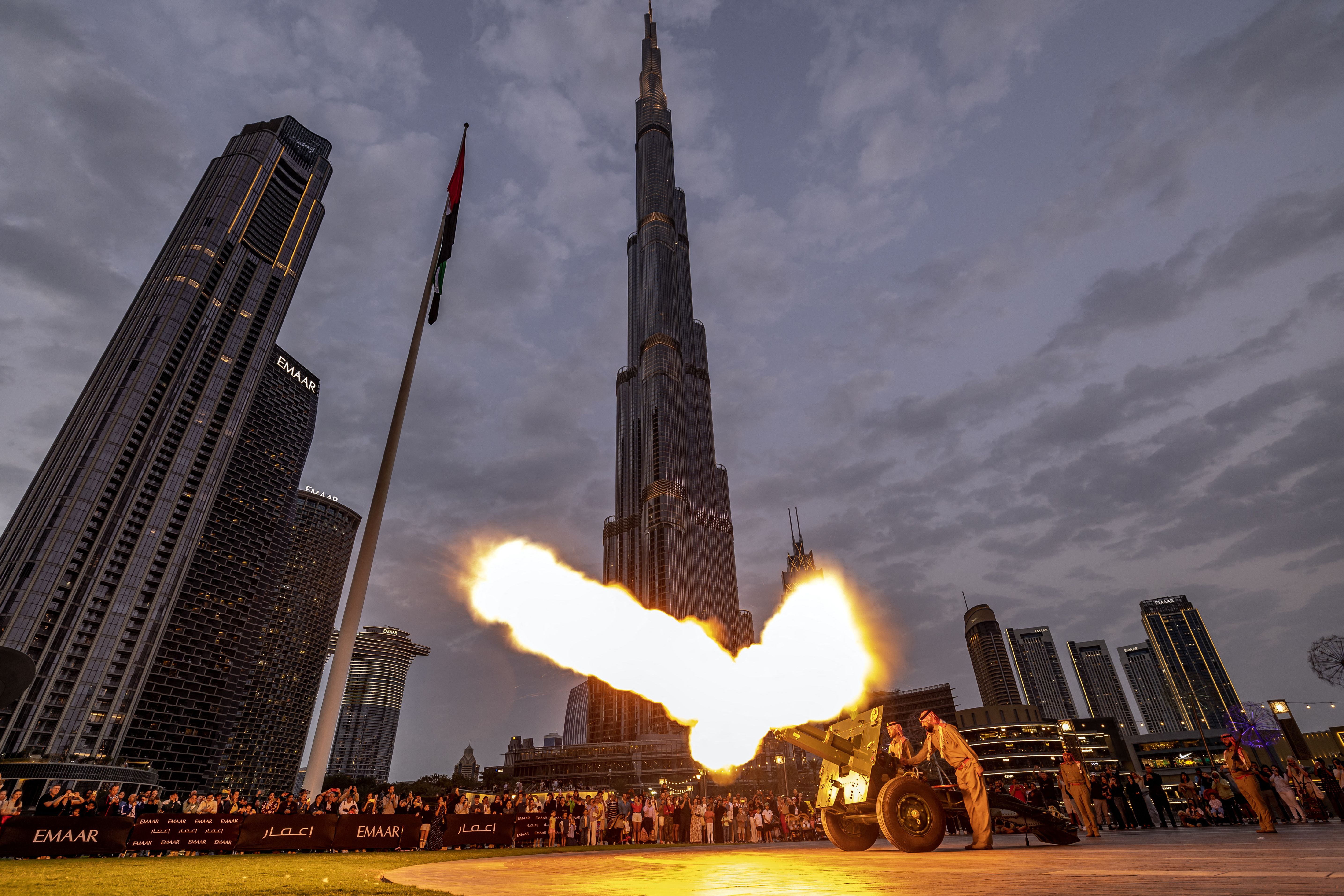  Emirati officers fire the iftar, or fast-breaking, cannon under a gray sky with tall buildings in the background