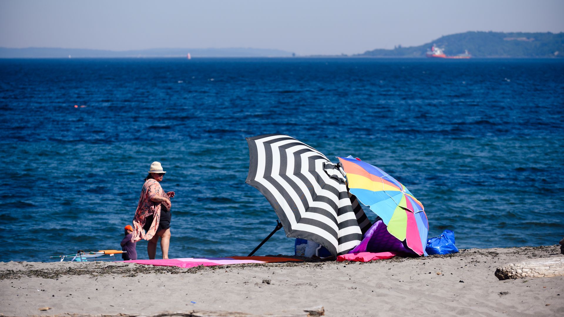 A person stands next to colorful beach umbrellas on Seattle's Alki Beach. 