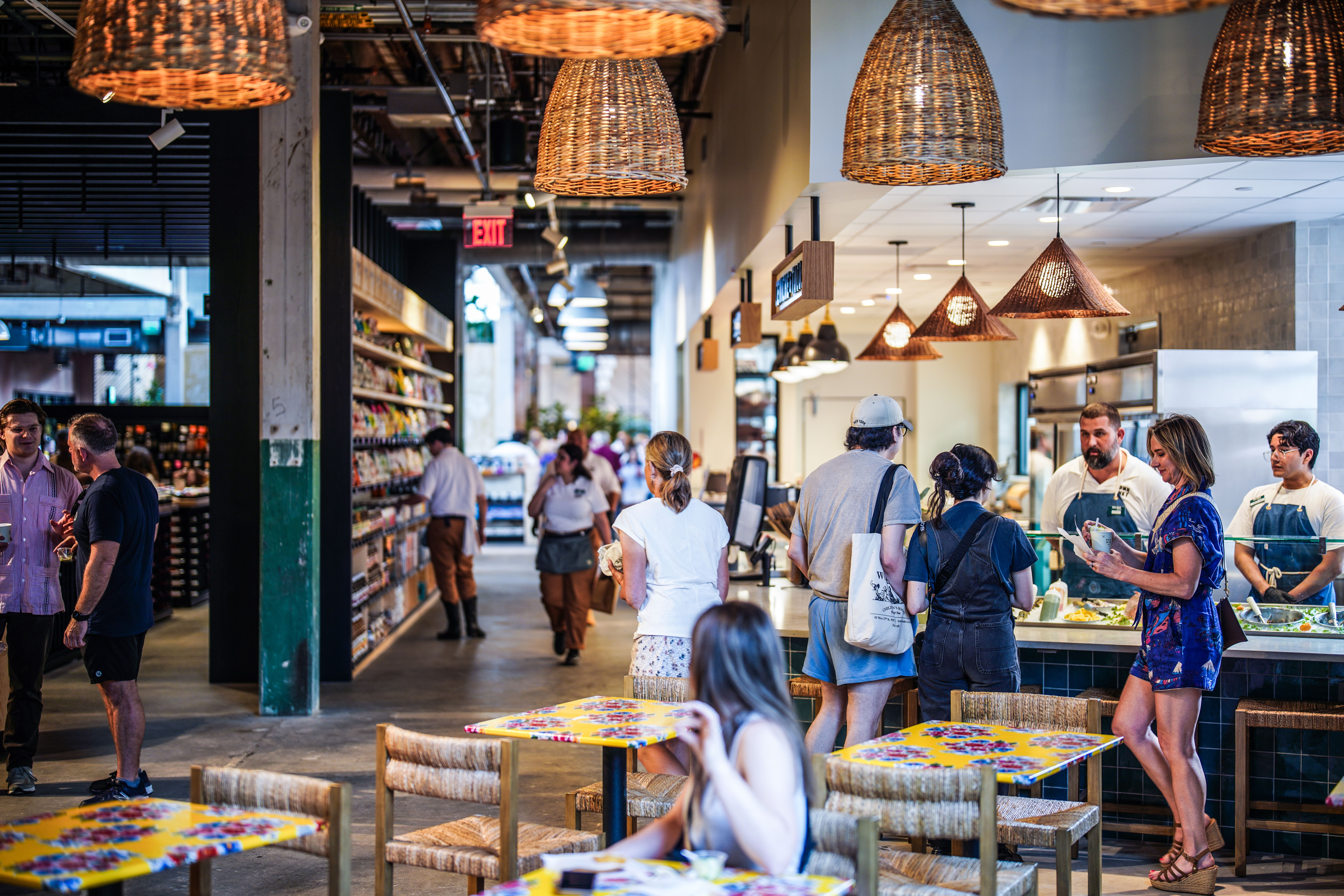 Shoppers peruse grab-and-go kiosks under rattan light fixtures.