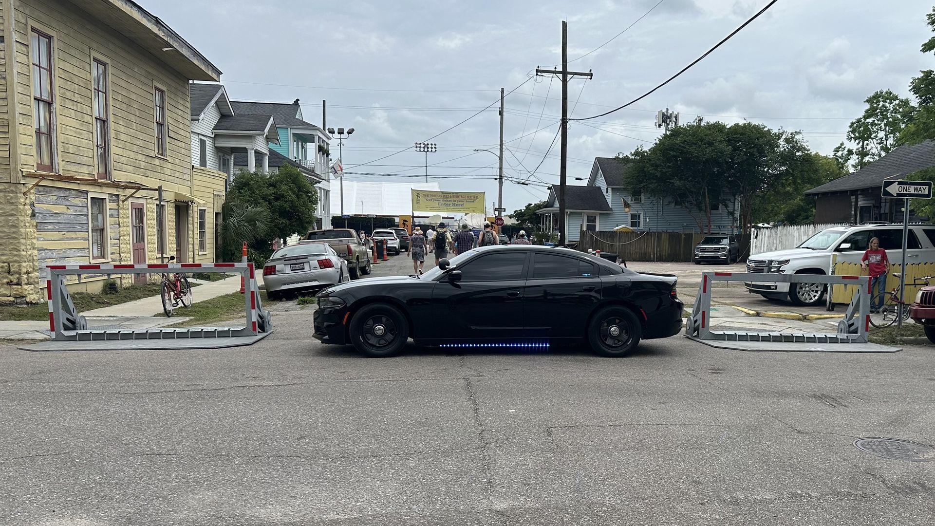 A black police car blocks a street with two large gray barricades to either side of it.