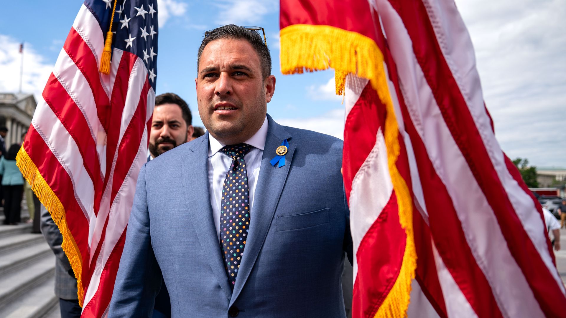Rep. D'Esposito, wearing a blue suit and holding an American flag outside.