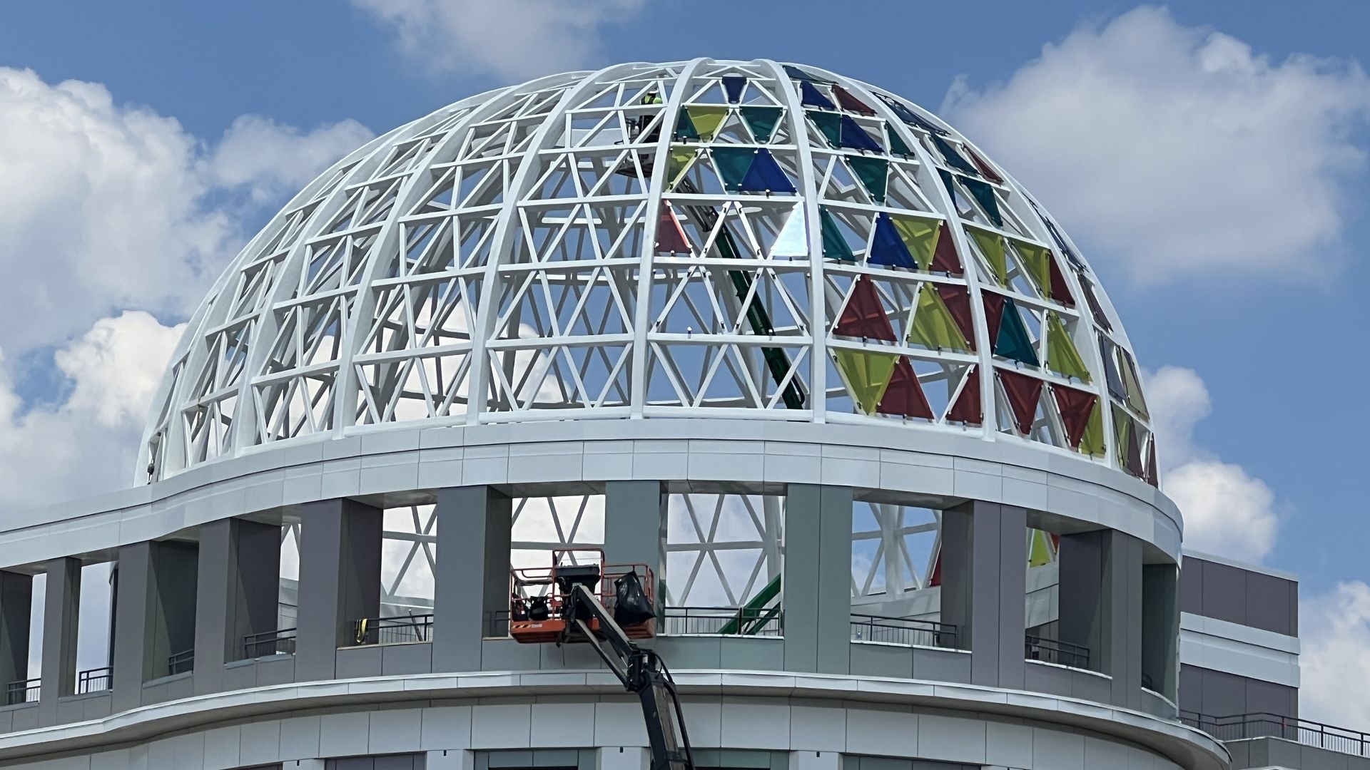 A construction worker in a cherry picker removes colorful glass triangles from a dome at a public building
