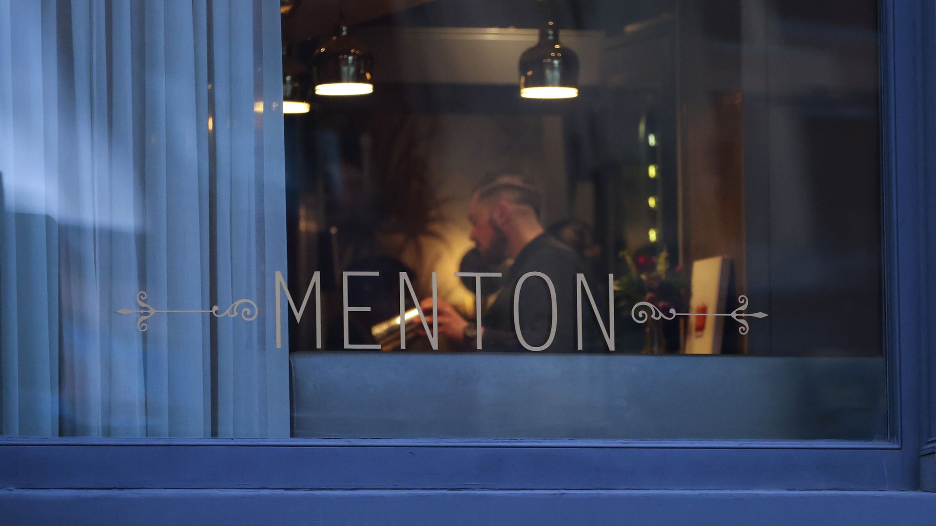 A photo looking into the window of Menton, a Boston restaurant owned by Barbara Lynch, with diners sitting in the background/restaurant.