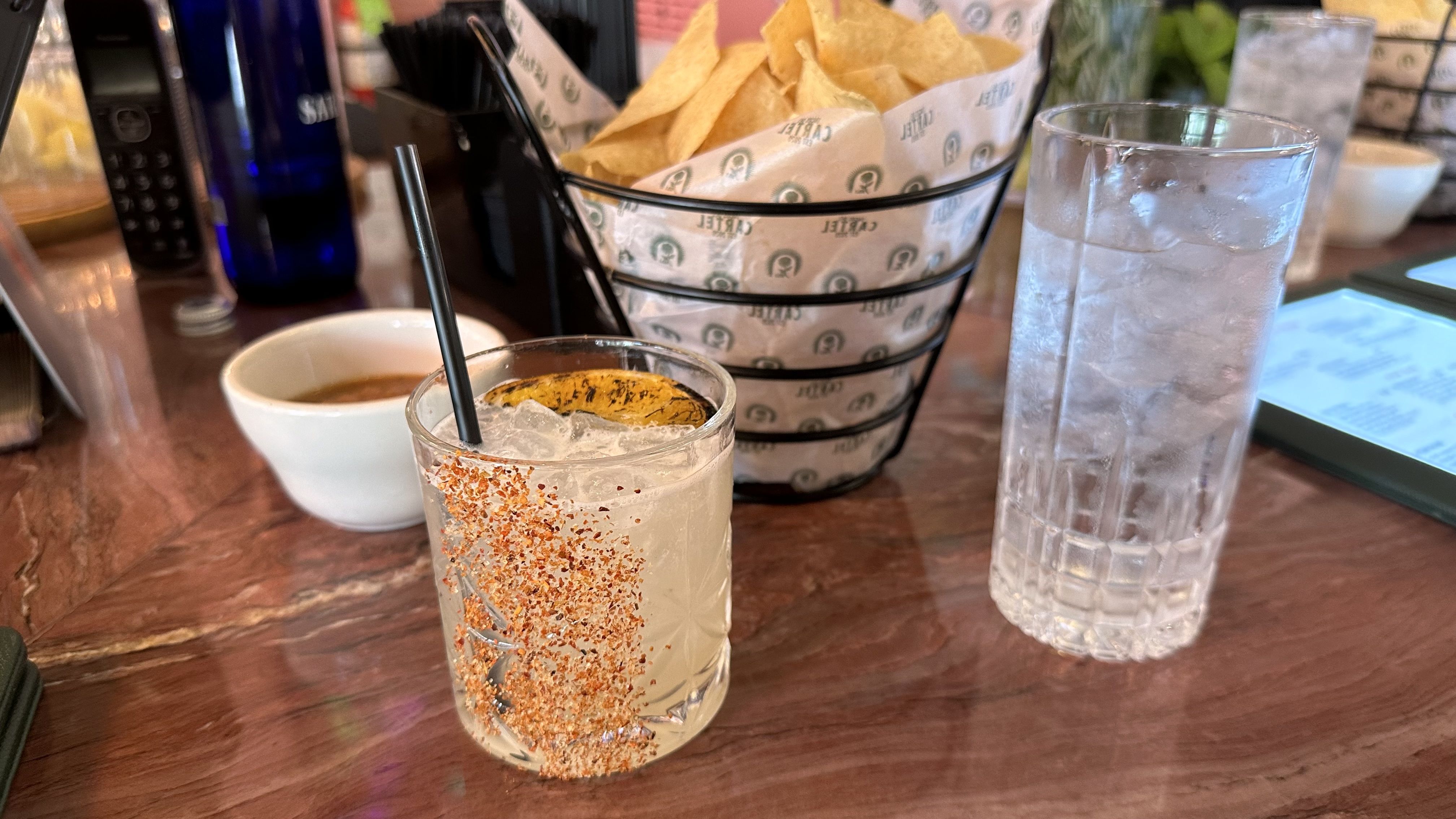 A margarita sits on a bar top. One side of it has been dipped in Tajin.
